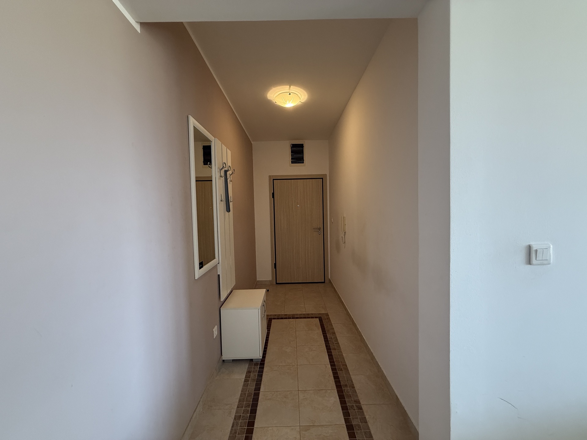 Bright entryway in an apartment in Budva, Montenegro: tiled floor, mirror, coat rack, and a modern-style front door.