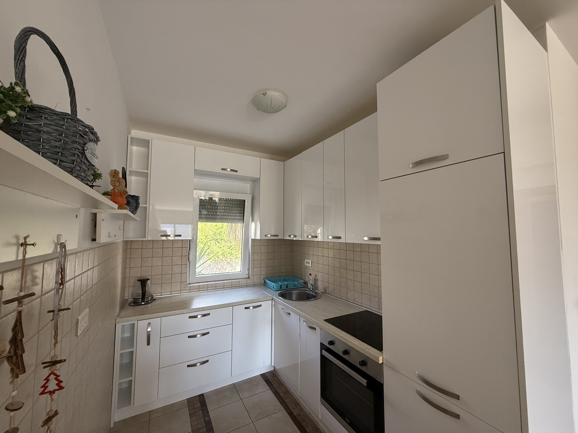 Modern white kitchen in an apartment in Budva, Montenegro: built-in appliances, glossy fronts, and a window with a view.