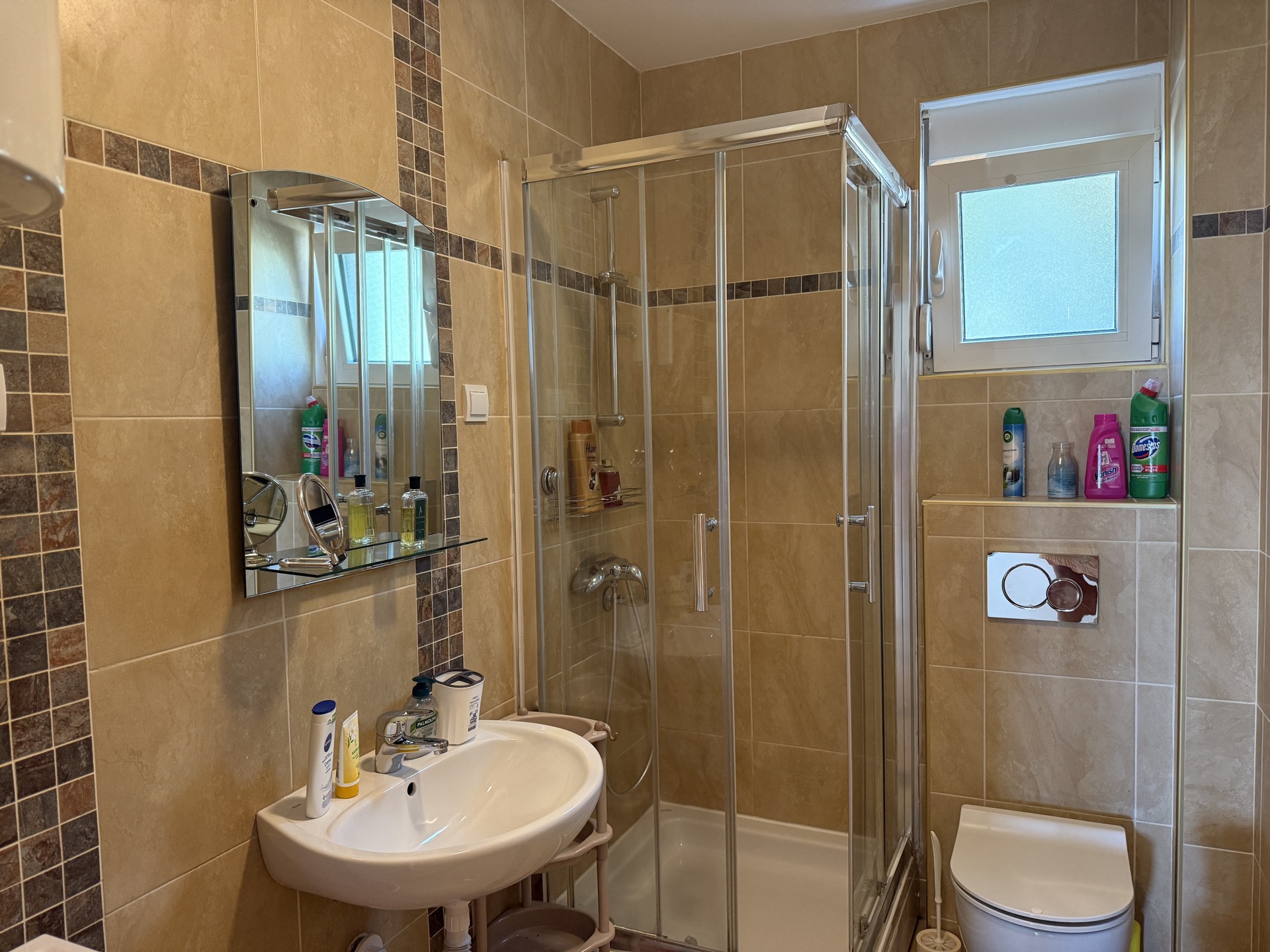 Bathroom in an apartment in Budva, Montenegro: shower cabin, sink, mirror, and tiled wall finish.