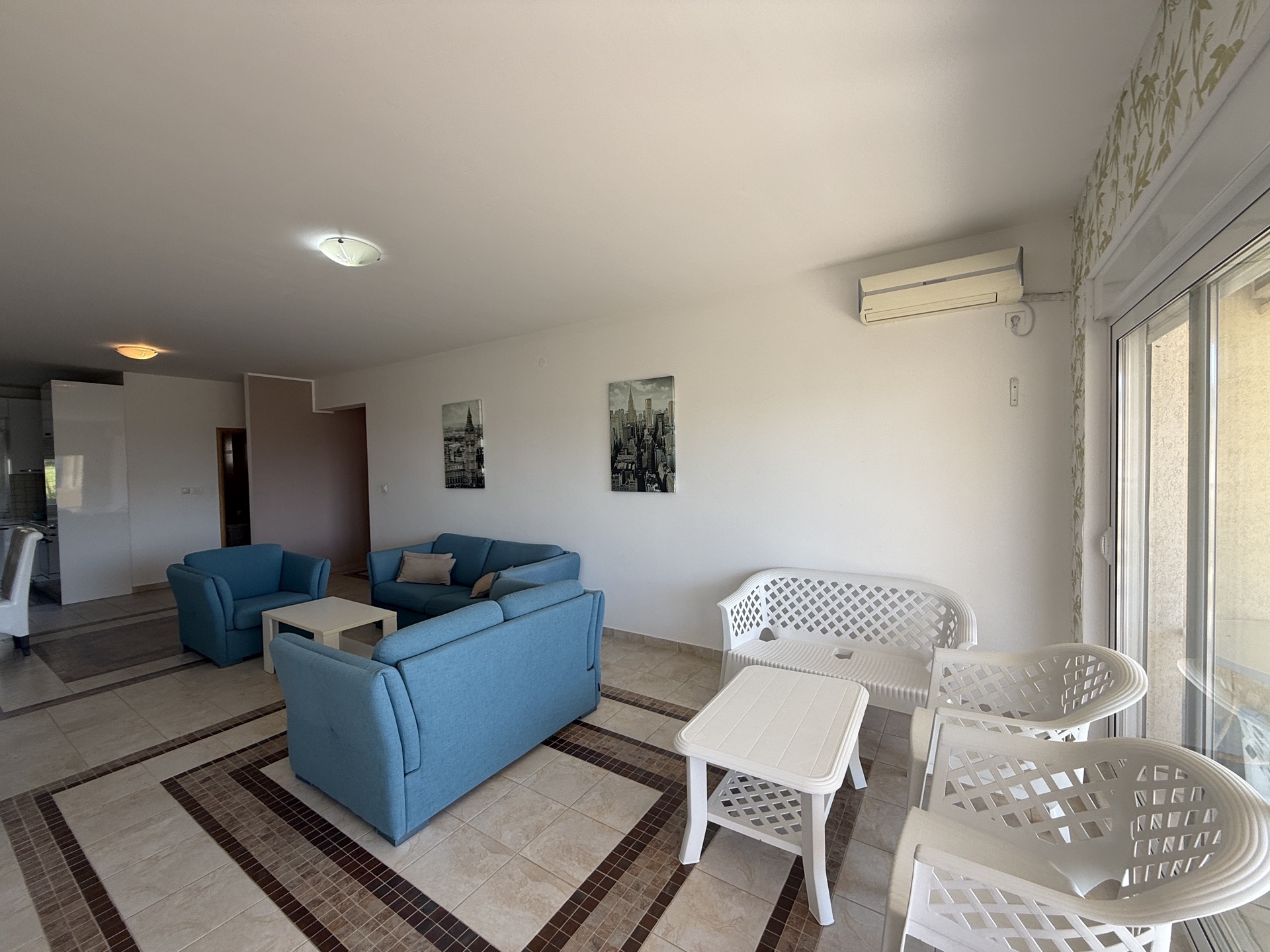 Living room in an apartment in Budva, Montenegro: blue sofas, white plastic furniture, and access to the terrace.