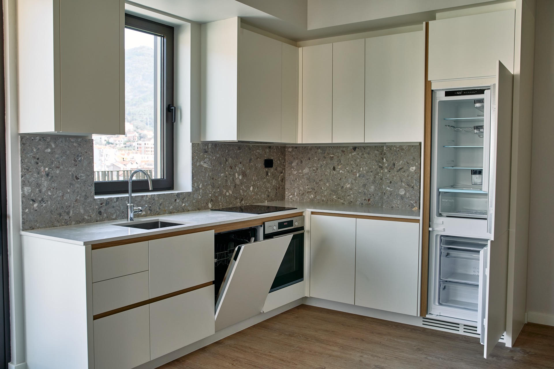 Modern kitchen in an apartment, Tivat, Montenegro: built-in appliances, stone backsplash, and mountain view from the window.