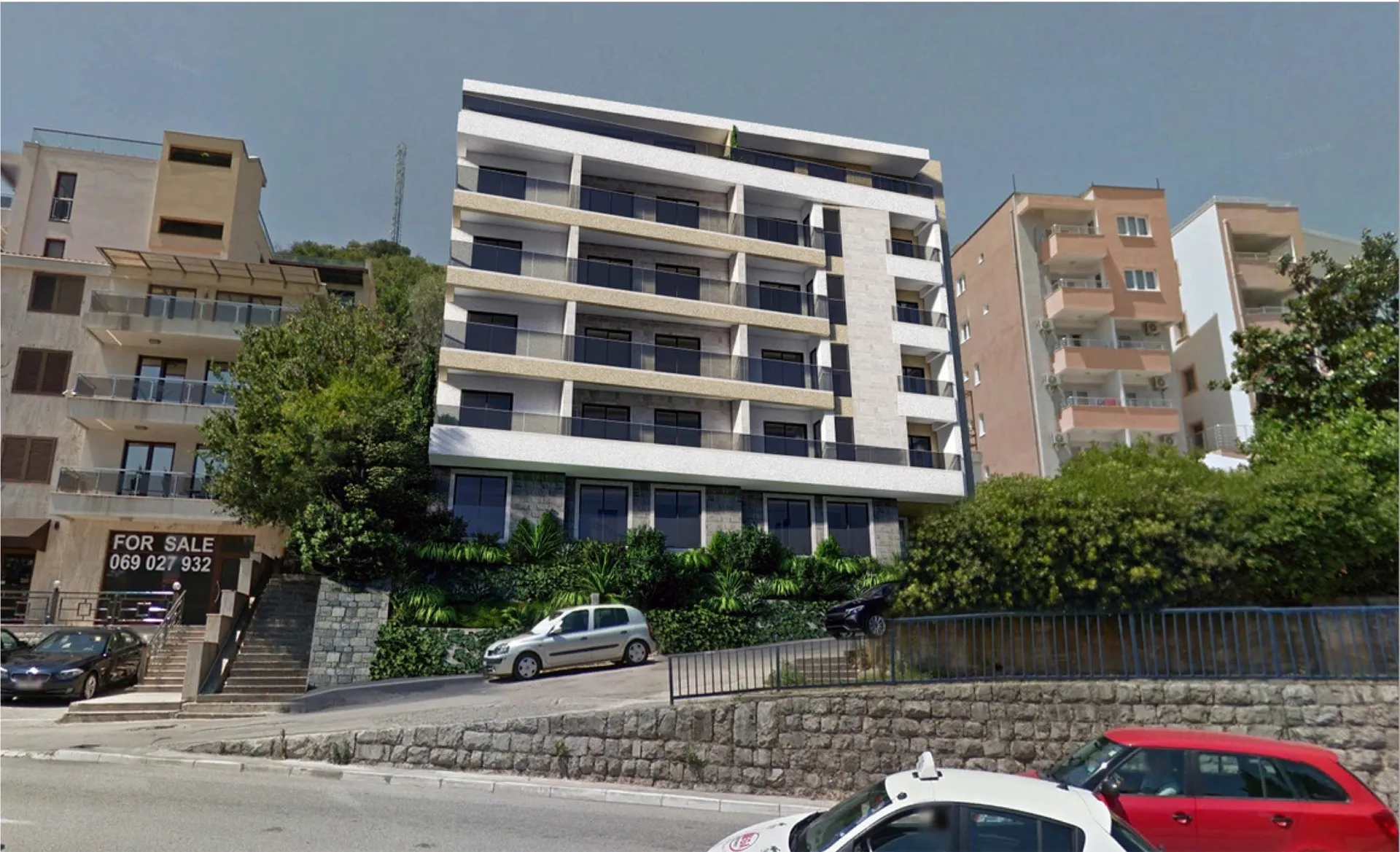 Modern multi-story residential building with balconies and glass railings on a hillside.