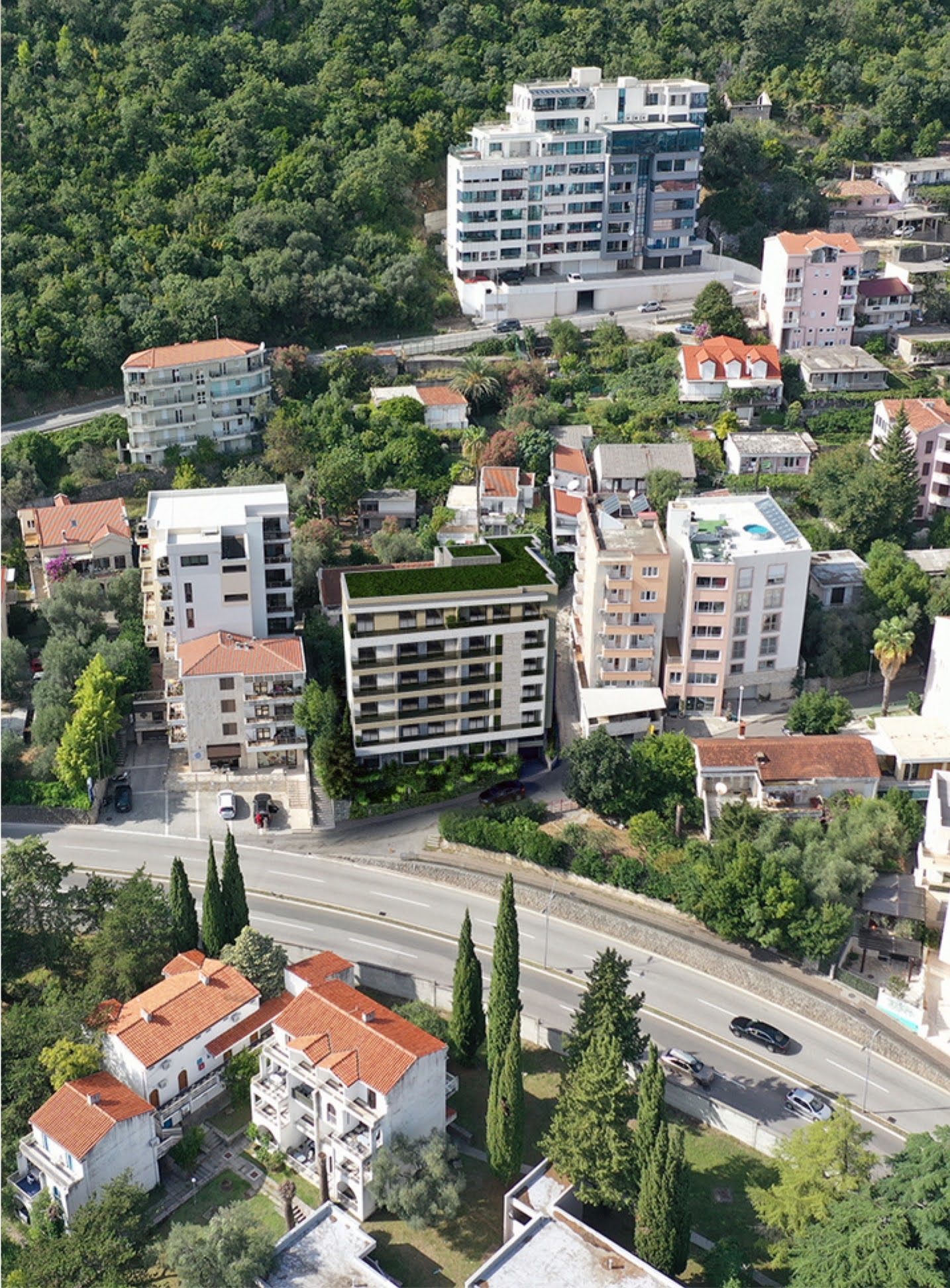 Aerial view of a modern residential complex in Bečići, Montenegro, nestled among green hills and urban development.