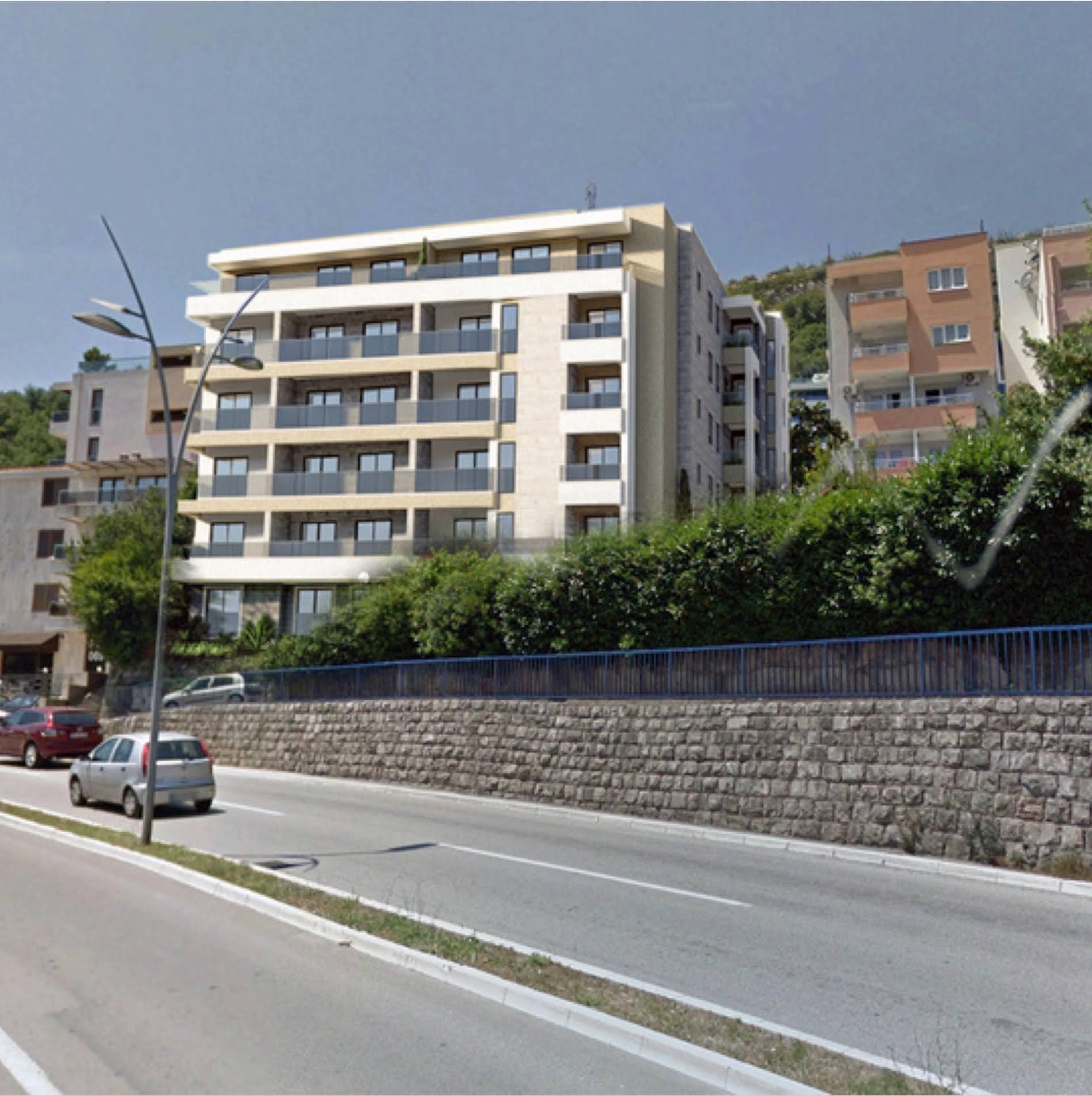 Modern residential complex with balconies in Bečići, Montenegro: view of the building facade from the road with a stone retaining wall