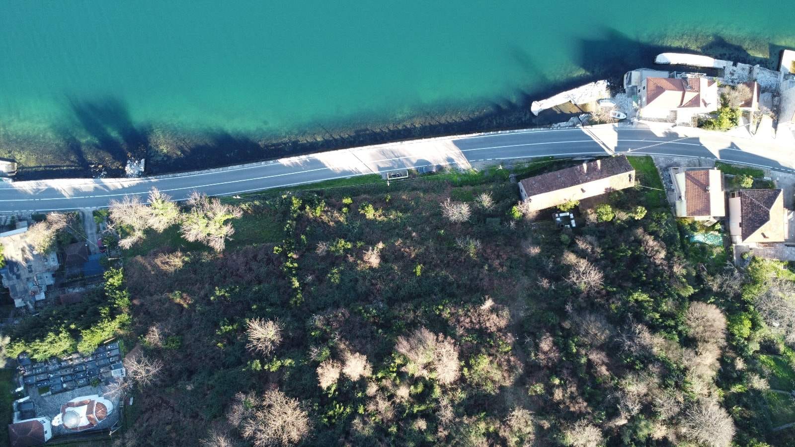 Aerial view of a development site in Kostanica, Montenegro: coastline, road, and houses by the sea.