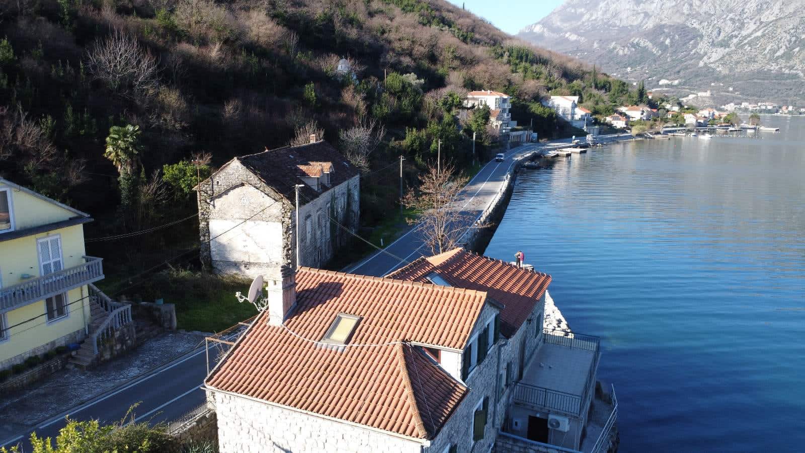 Stone house with a tiled roof on the seafront in Kostanica, Montenegro: aerial view of the coast and mountains.