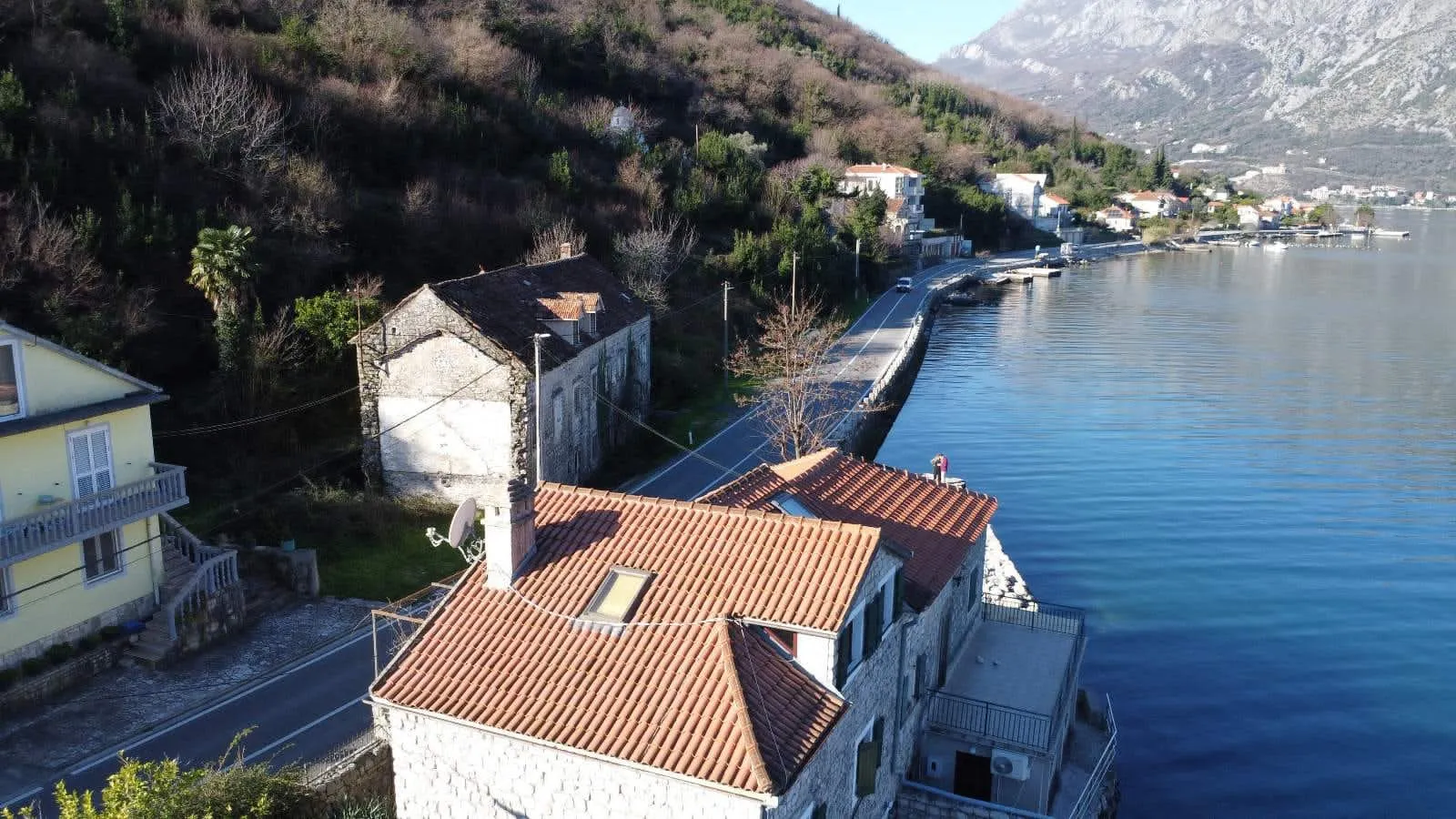 Aerial view of stone houses with red tile roofs located next to the sea and a mountain slope.
