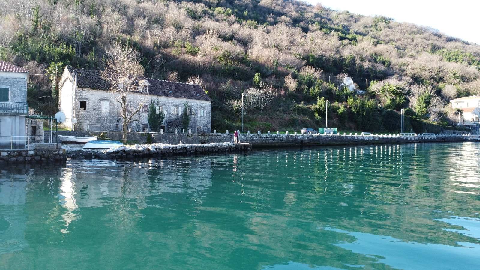 Stone house on the seafront in Kostanica, Montenegro: view of an old building by the water and the mountains.