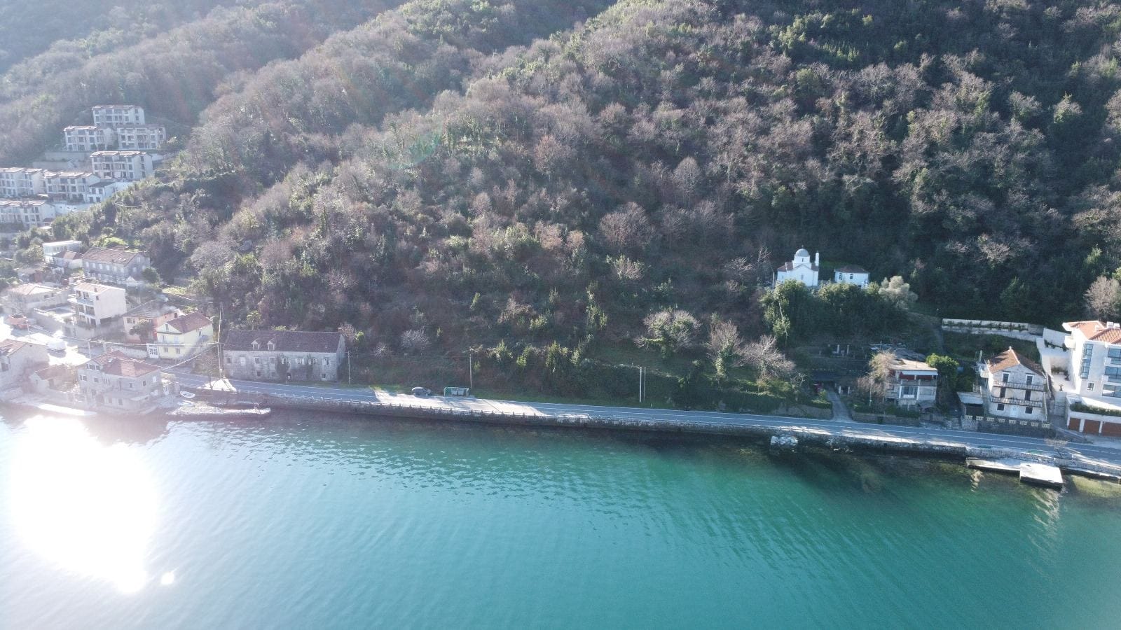 Aerial view of a coastal plot and houses in Kostanica, Montenegro: a panorama of the sea, mountain slope, and historic buildings.