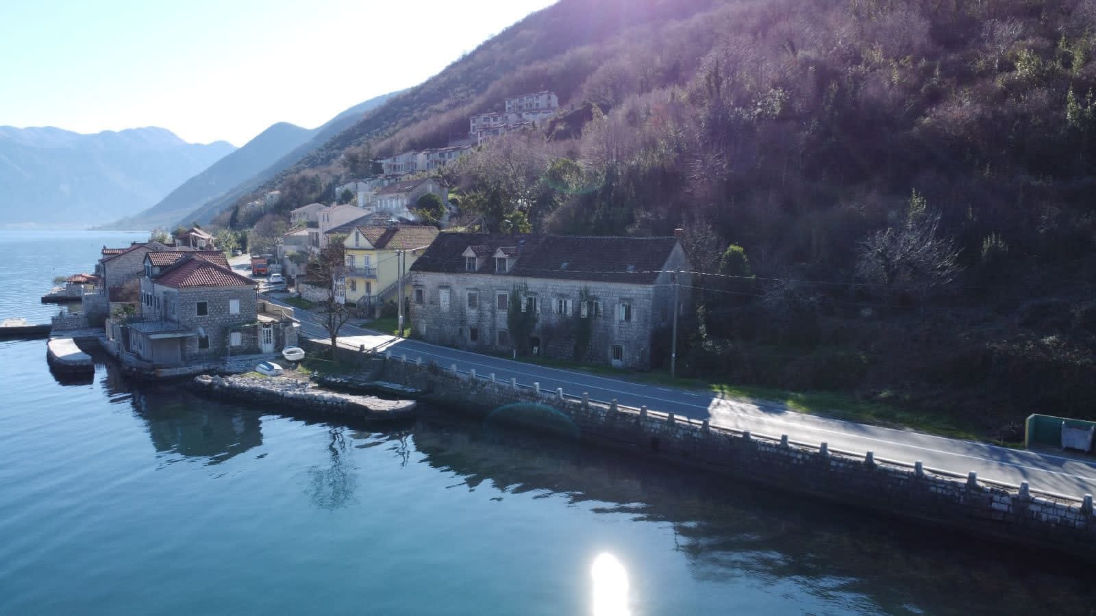 Stone house on the seafront in Kostanjica, Montenegro: view of an old building by the water and a mountain landscape.