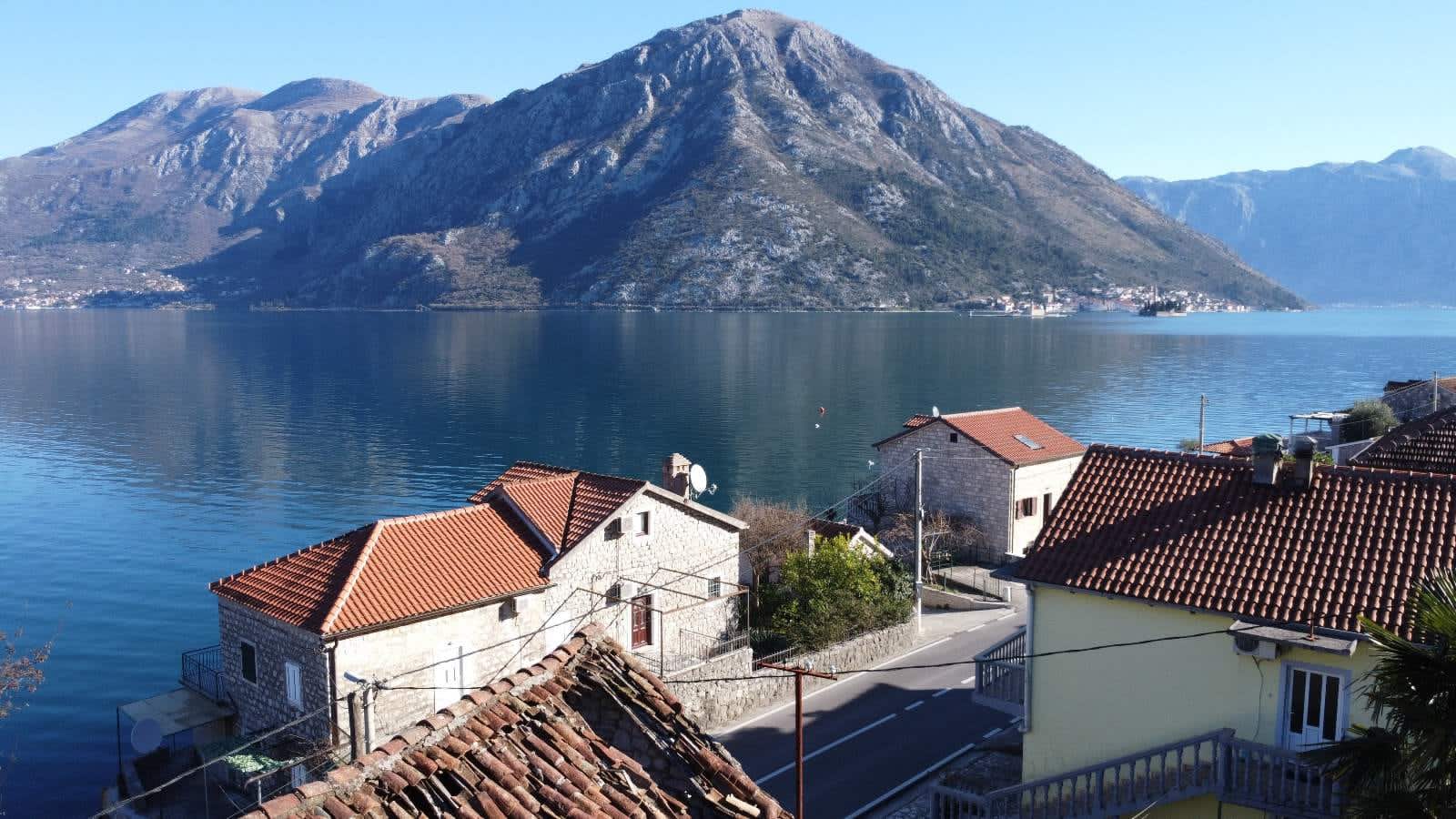Panoramic view of the Bay of Kotor and mountains from a house in Kostanjica, Montenegro: stone buildings with tiled roofs.
