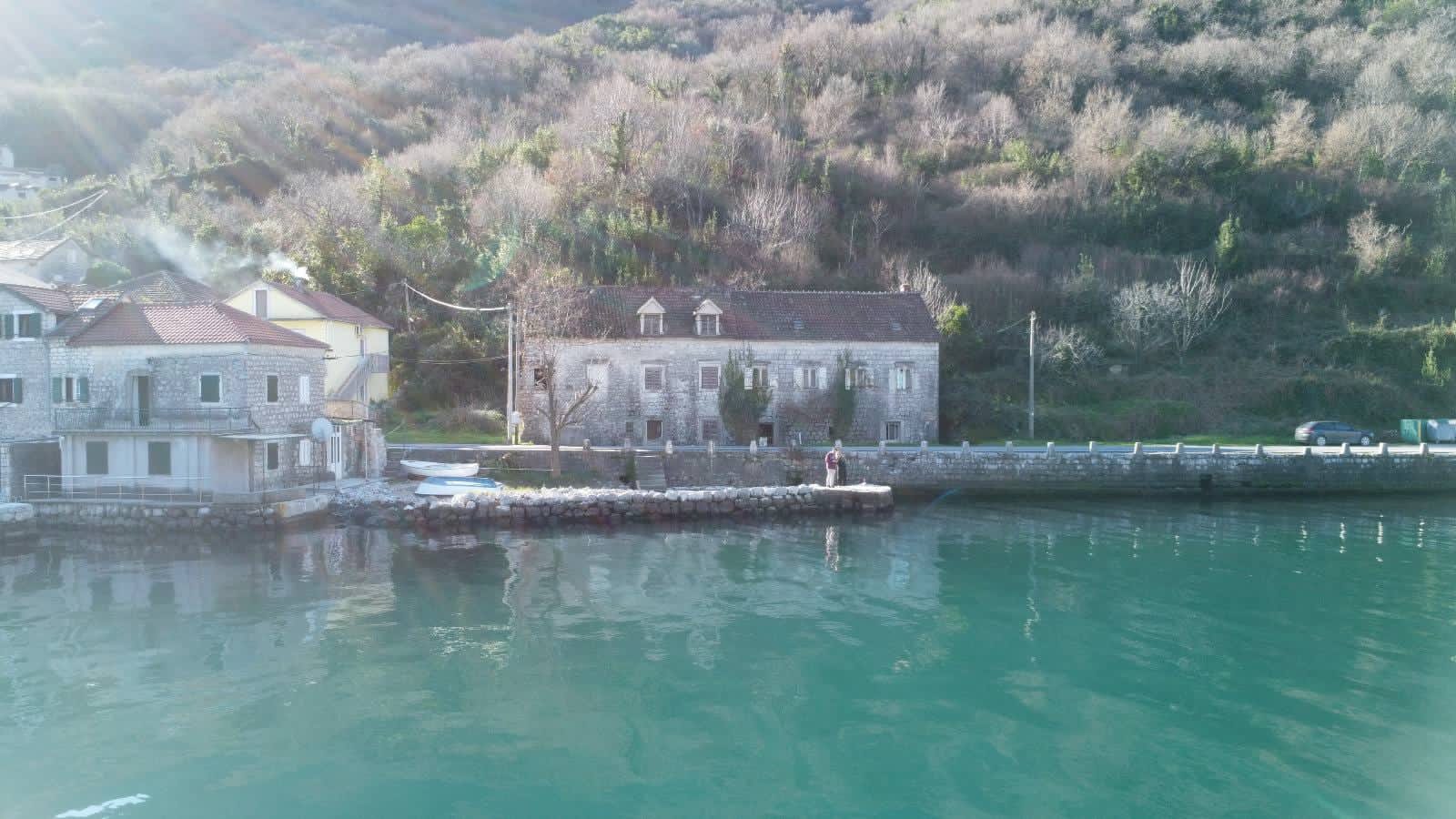 An old stone house on the seafront in Kostanjica, Montenegro: view of the facade and a private waterfront pier.