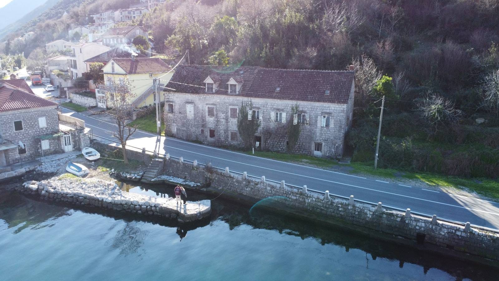 An old stone house on the seafront in Kostanjica, Montenegro, aerial view of the pier and coastline.