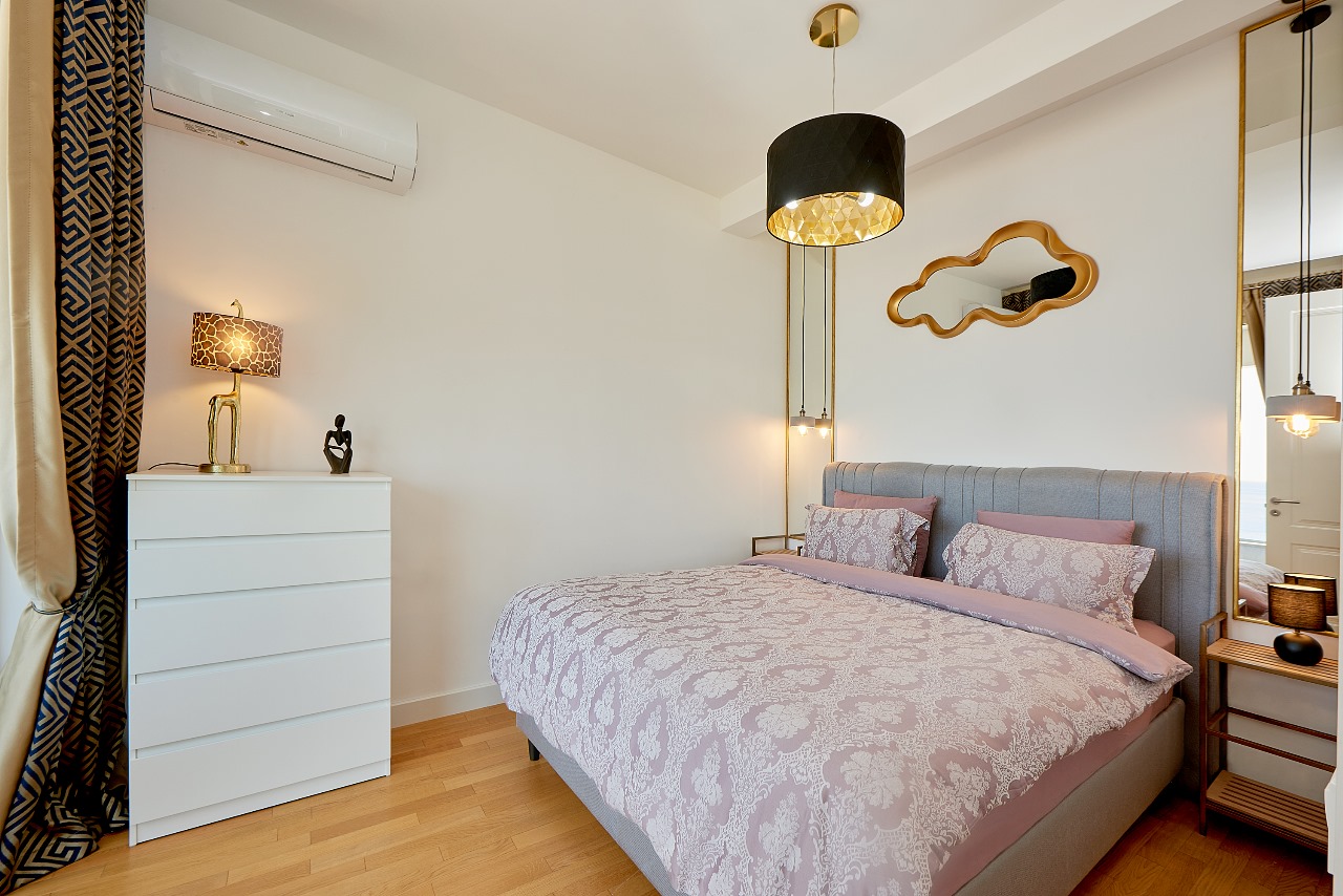 Modern bedroom in an apartment in Bečići, Montenegro: double bed, white dresser, stylish lighting and decor.