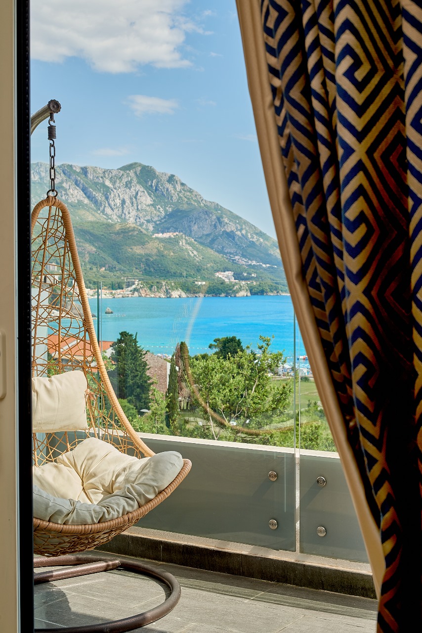 Balcony with a wicker cocoon chair and panoramic sea and mountain views in an apartment, Becici, Montenegro.