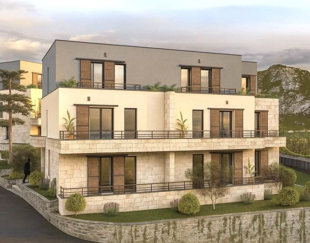 Modern three-story building with stone facade, balconies, and wooden elements set against a mountain backdrop.