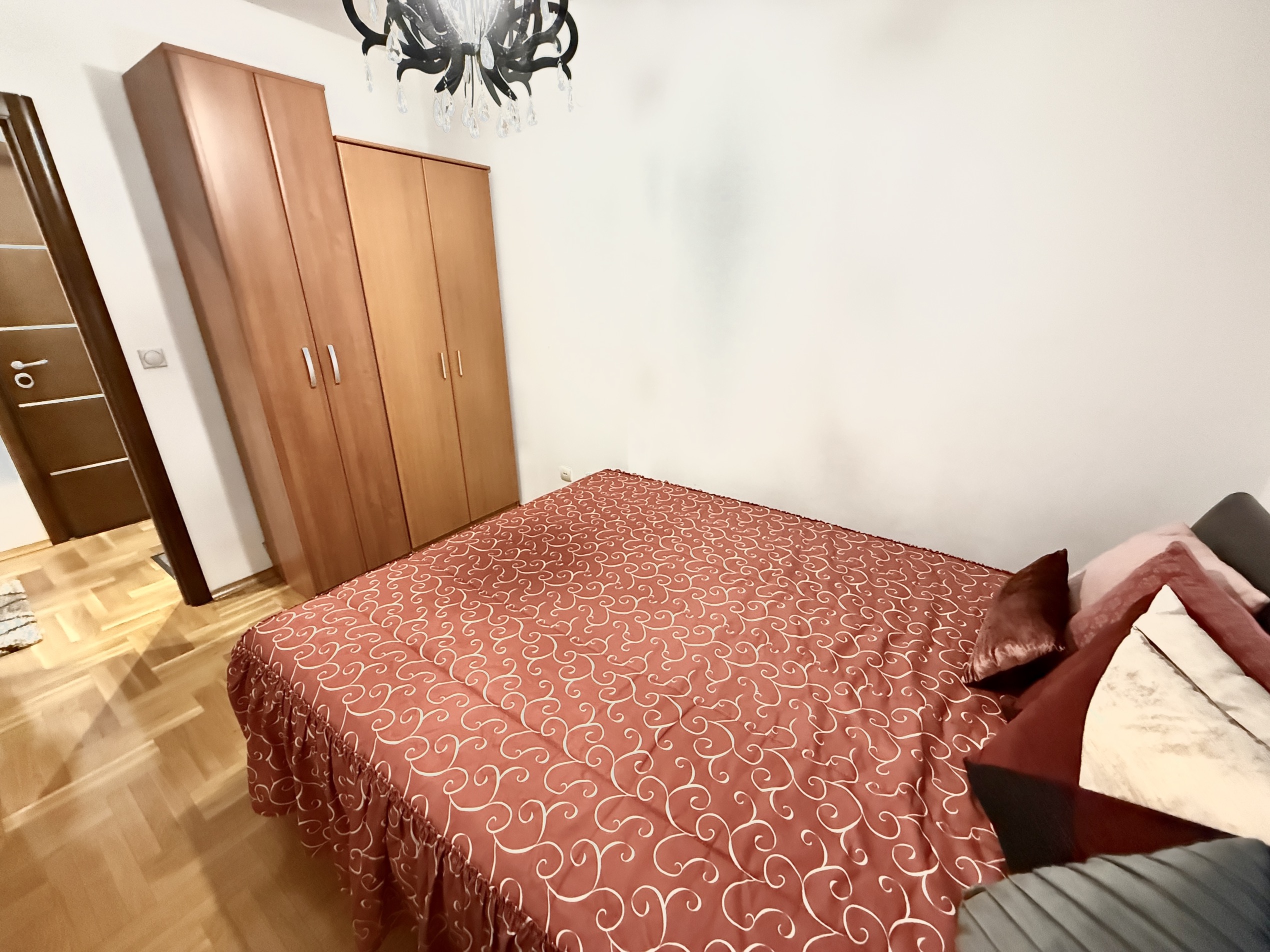 Bedroom in an apartment in Budva, Montenegro: a double bed with a red bedspread, a wooden wardrobe, and parquet flooring.