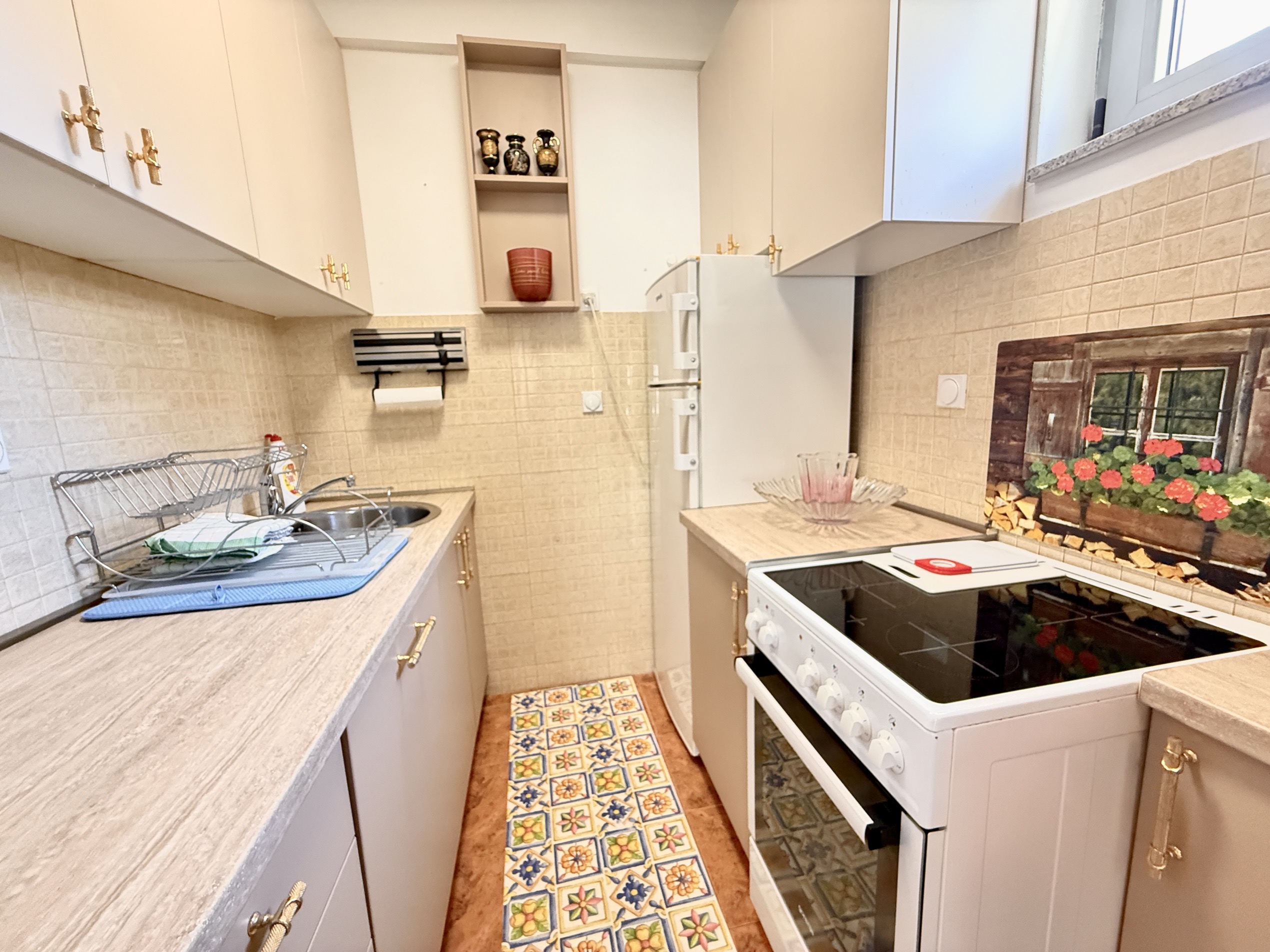 Compact kitchen in an apartment in Budva, Montenegro: light-colored cabinets, stove, refrigerator, and decorative tile on the wall.