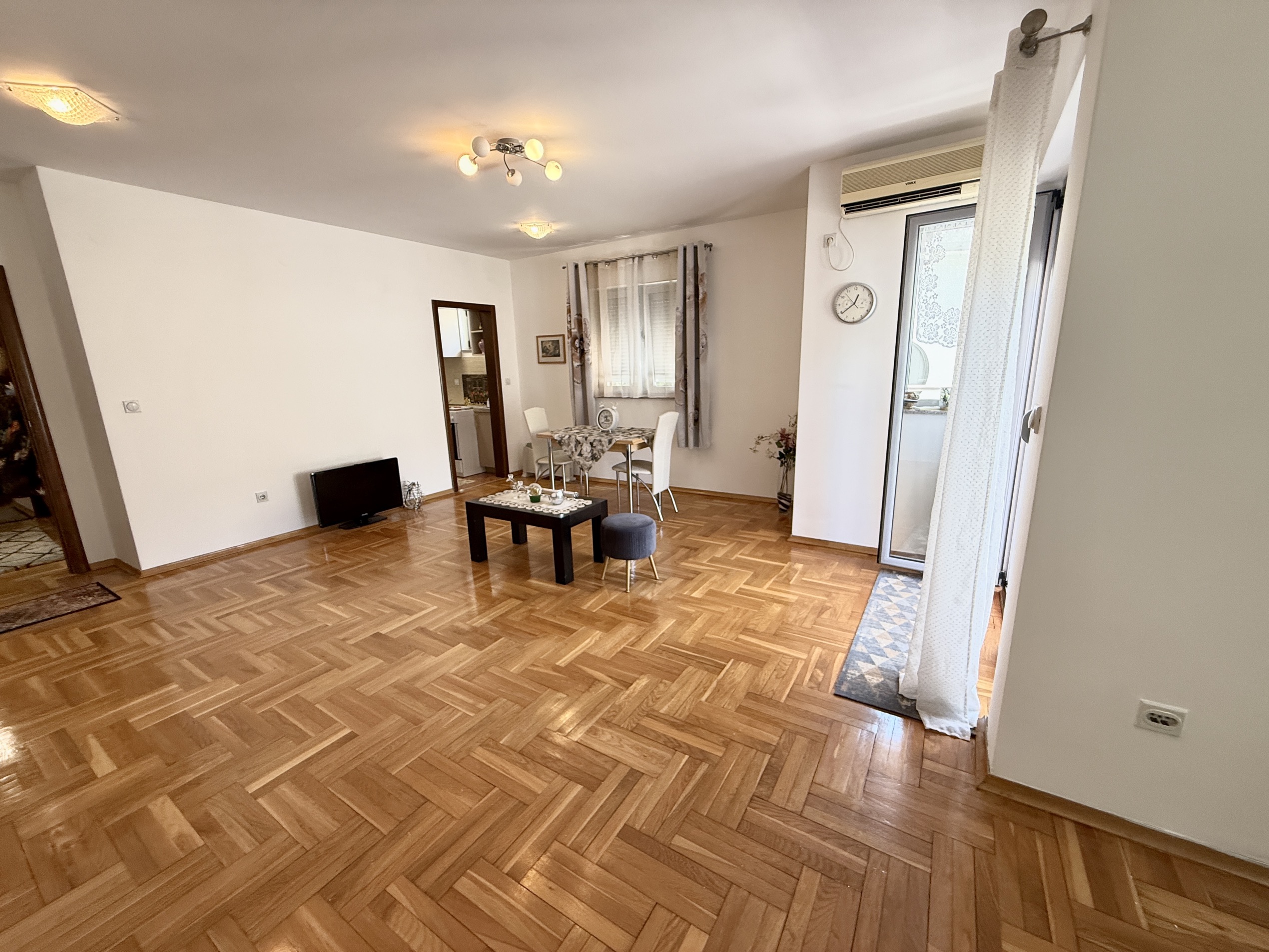 Spacious living room with parquet flooring and access to the balcony in an apartment, Budva, Montenegro. Furnished seating area and dining area.