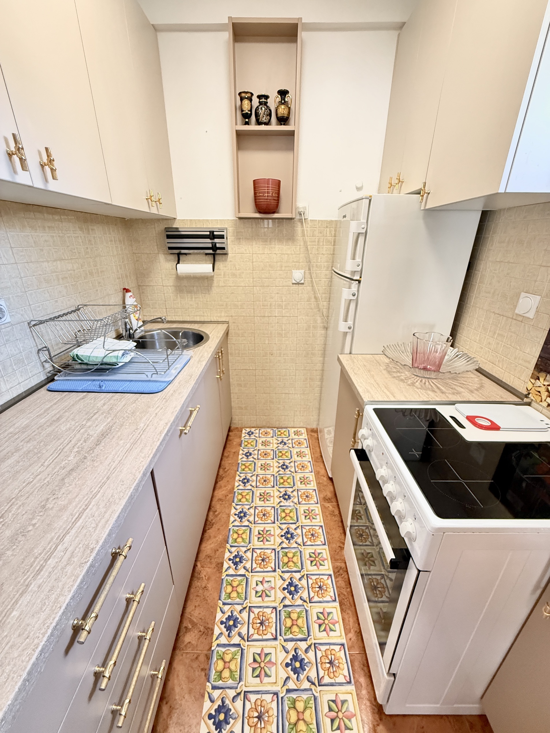 Compact kitchen in an apartment in Budva, Montenegro: light cabinets, stove, sink, and bright tiled floor decor.