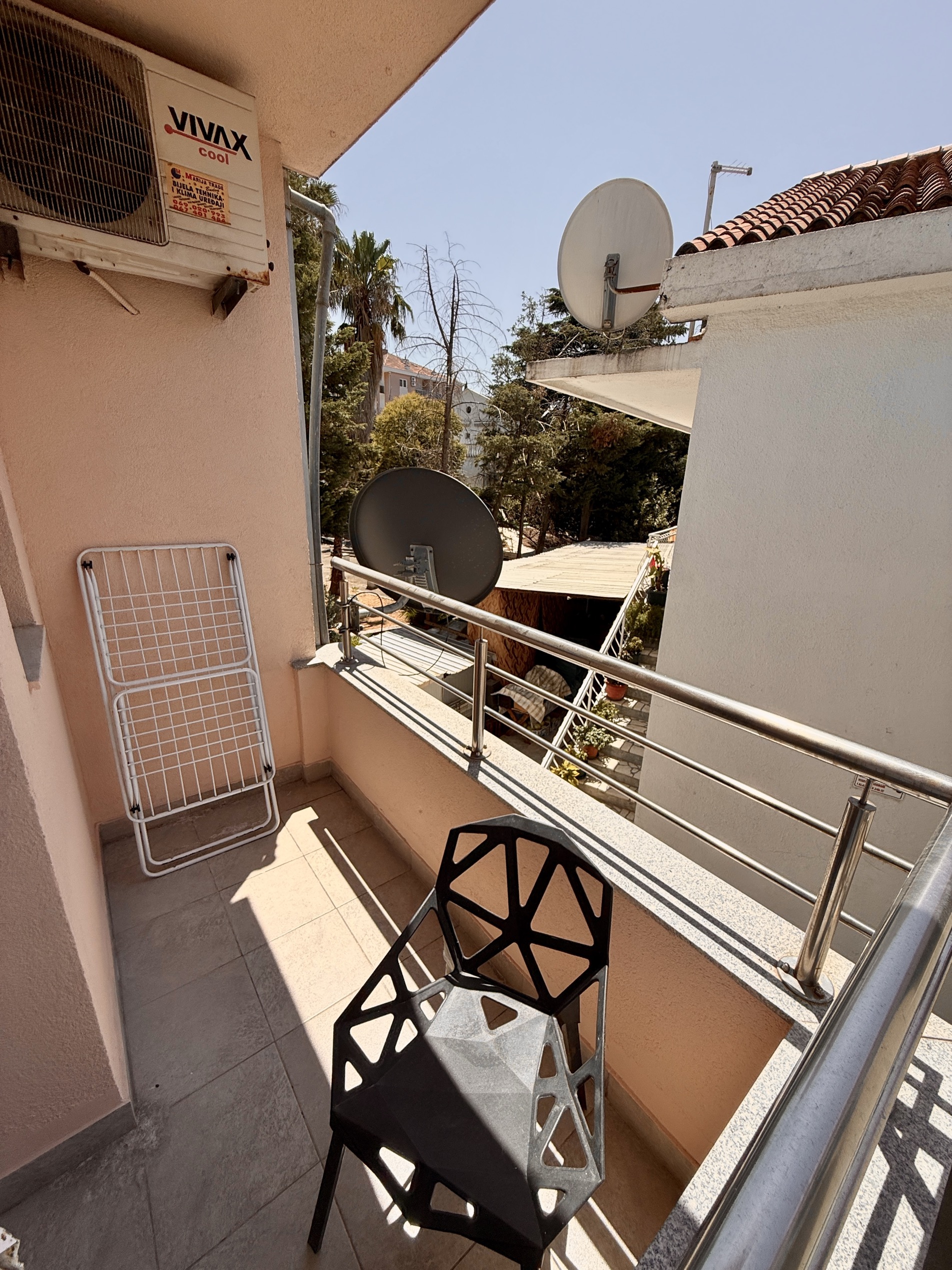 Apartment balcony in Budva, Montenegro: a modern chair, clothes drying rack, air conditioner, and view of a green courtyard.