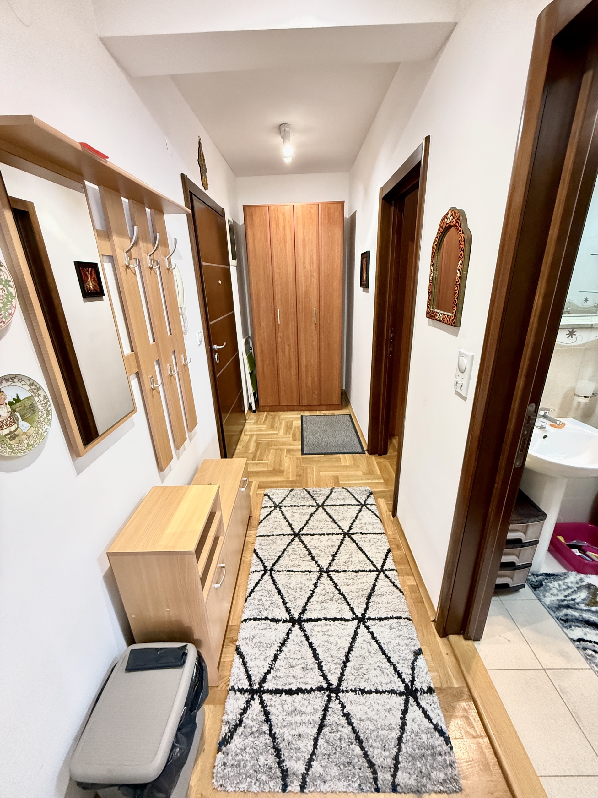 Bright hallway in an apartment in Budva, Montenegro: parquet floor, wooden cabinet, coat rack with mirror, and rug.