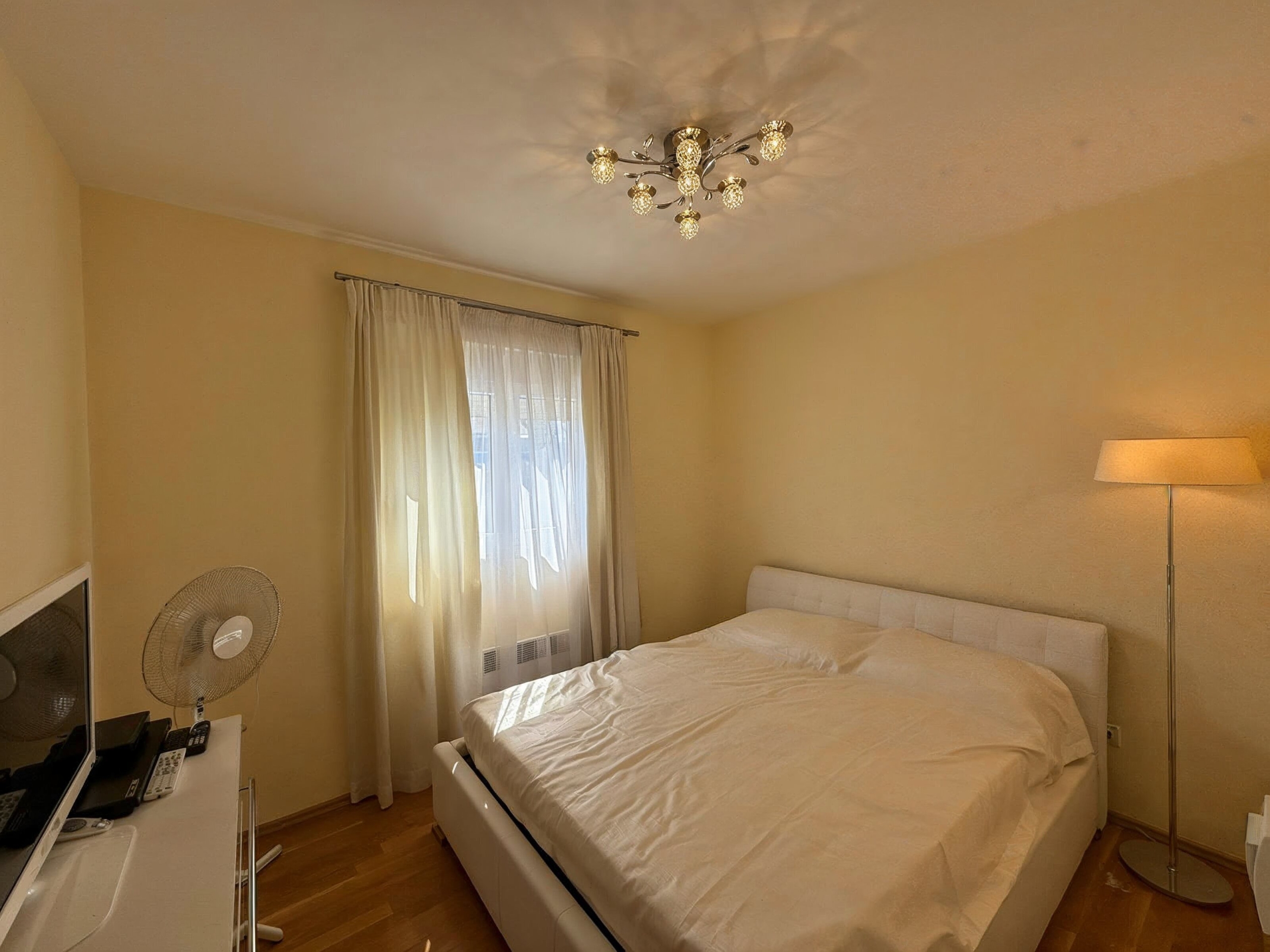 Cozy bedroom with a double bed in an apartment in Bečići, Montenegro: bright interior, parquet flooring, and a stylish chandelier.