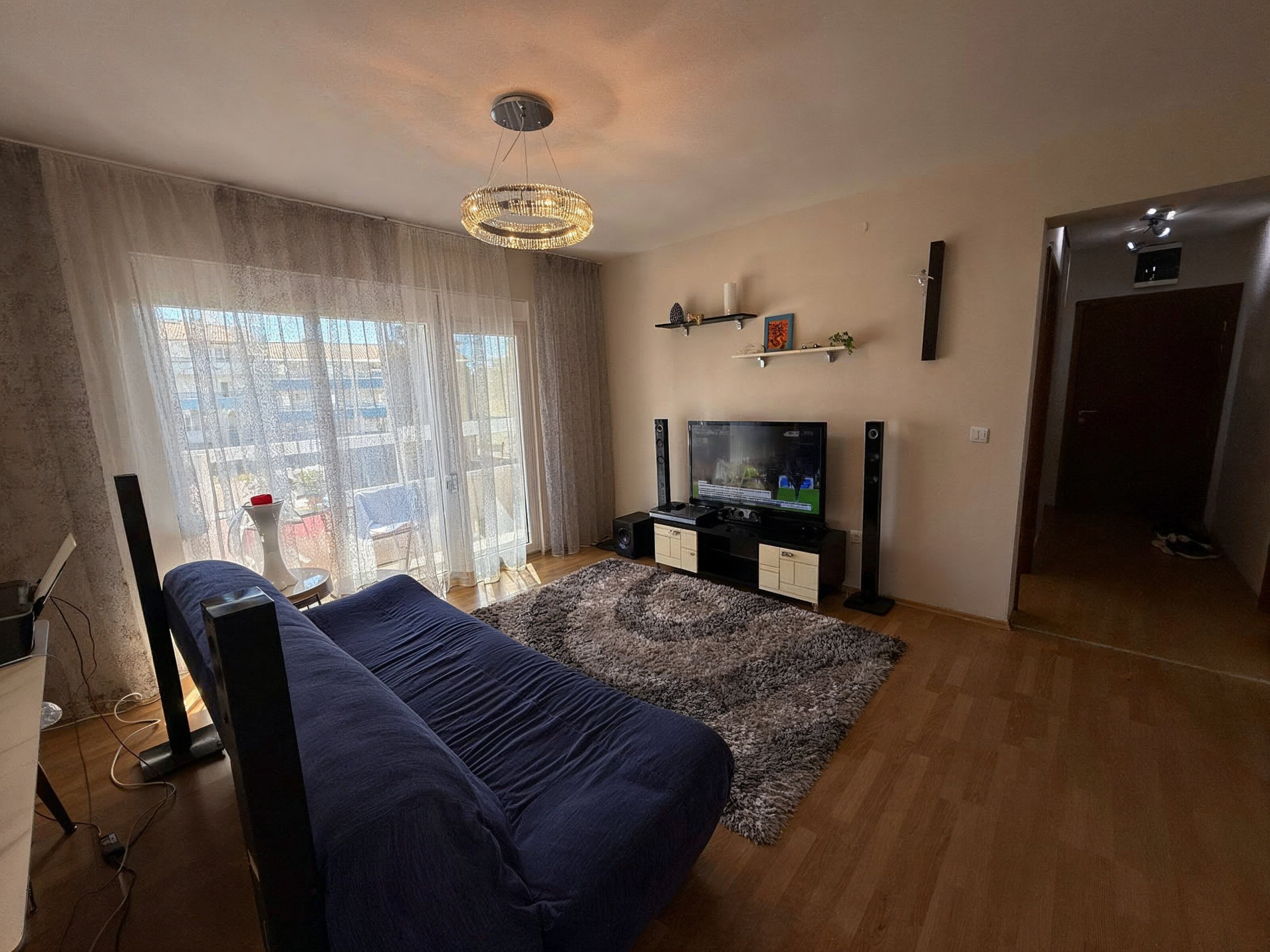 Cozy living room in an apartment in Bečići, Montenegro: blue sofa, TV area, panoramic window with access to the terrace.