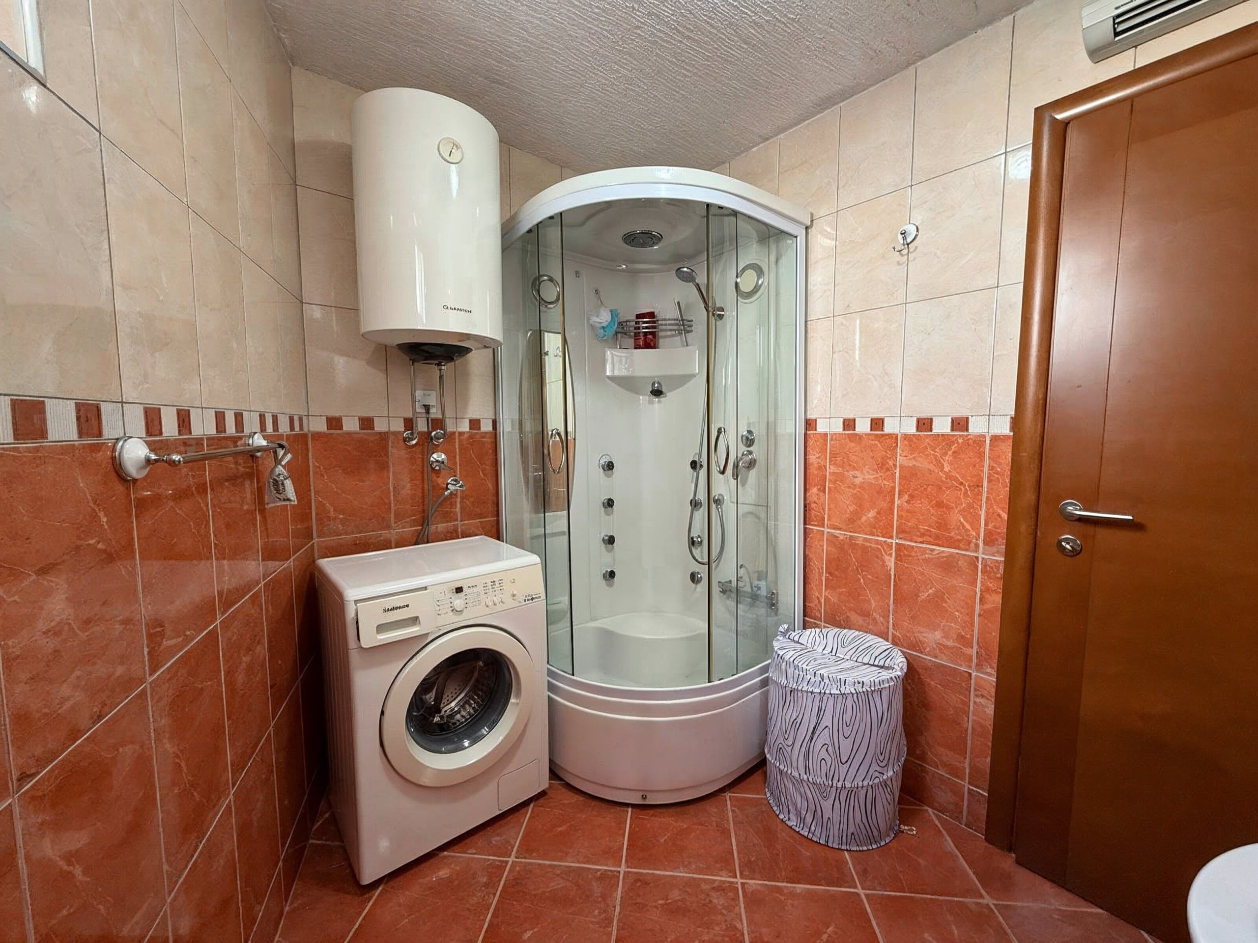 Bathroom in an apartment in Bečići, Montenegro: shower cabin, washing machine and water heater, tiled finish.