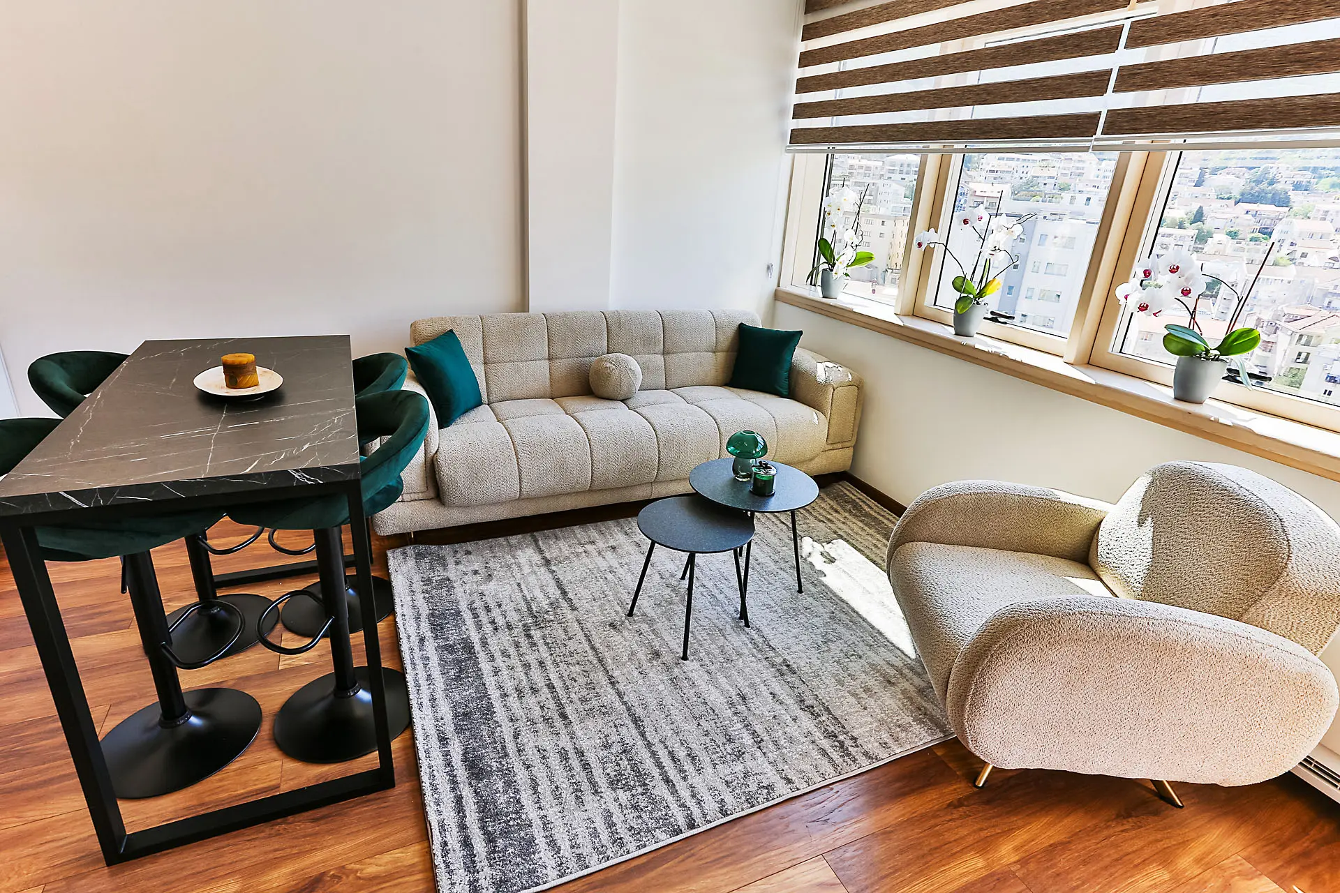 Modern living room in an apartment in Budva, Montenegro: beige sofa, armchair, dining table, and panoramic window view.