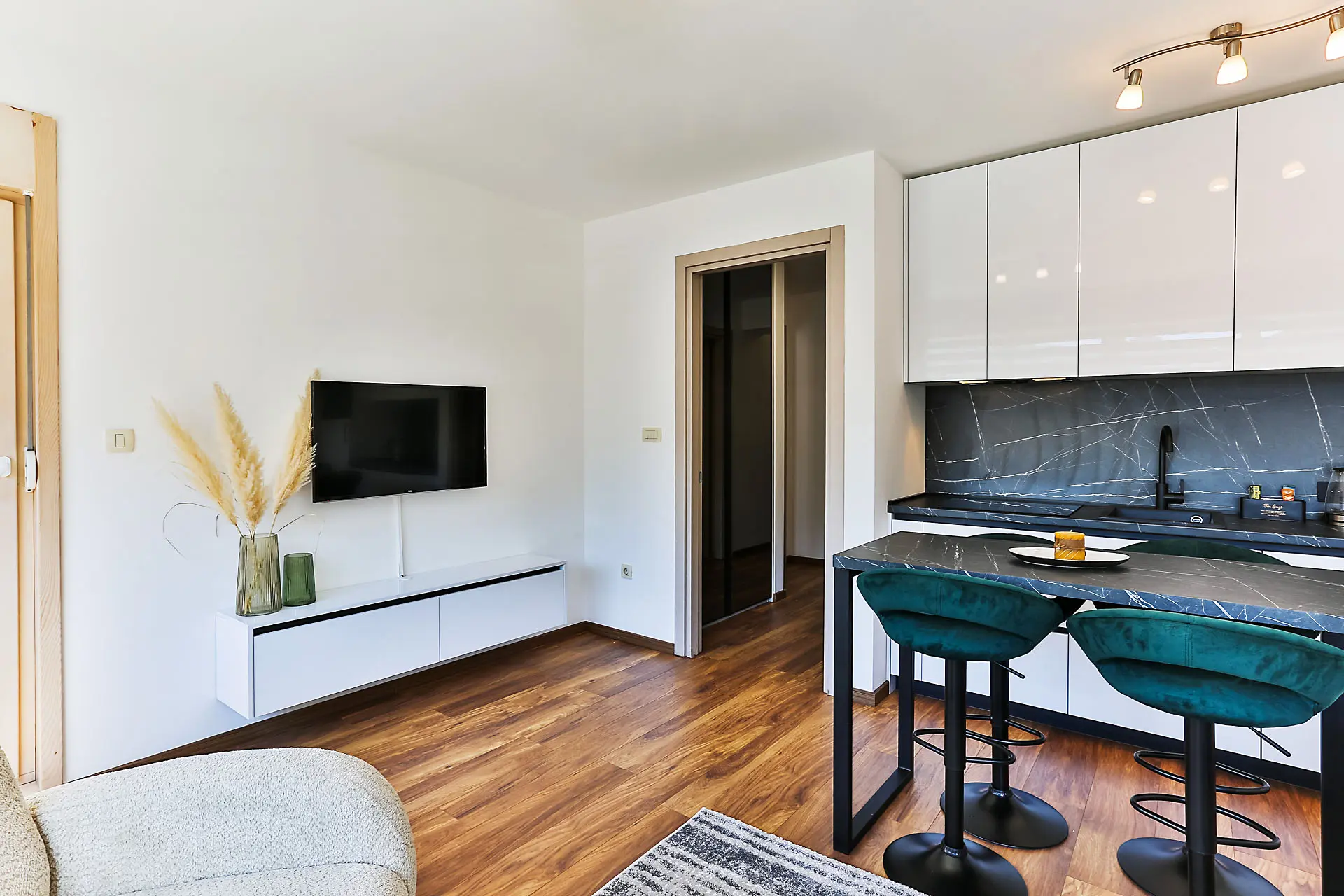 Modern living room with kitchen in an apartment in Budva, Montenegro: white furniture, a bar counter, and emerald chairs.