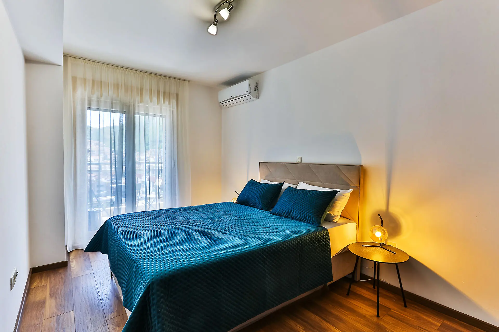 Modern bedroom with a double bed in an apartment in Budva, Montenegro: parquet flooring, air conditioning, and access to the balcony.