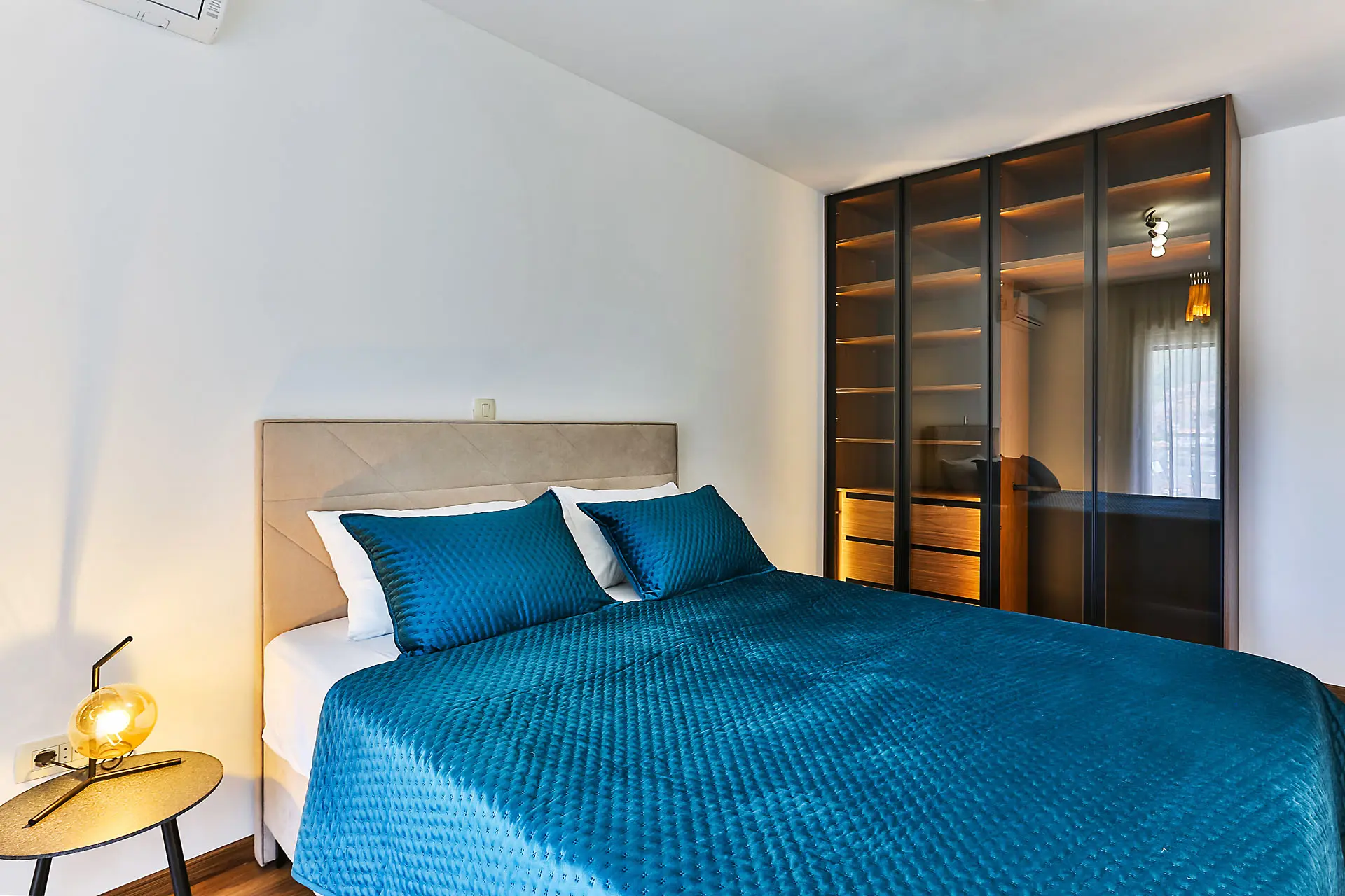 Modern bedroom in an apartment in Budva, Montenegro: double bed, blue bedspread, and a wardrobe with lighting.