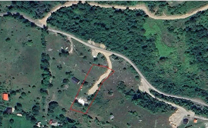 Aerial photo of a land plot outlined in red, surrounded by dense forest and winding dirt roads.