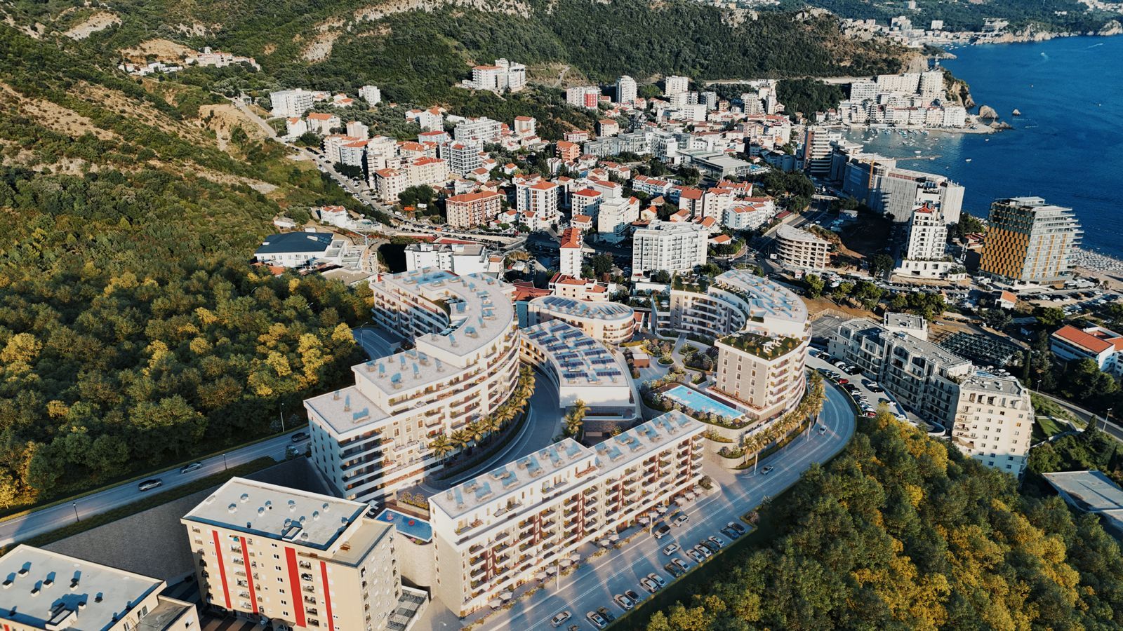 Aerial view of a residential complex in Bečići, Montenegro: modern buildings, a swimming pool, and a panoramic view of the Adriatic coast.
