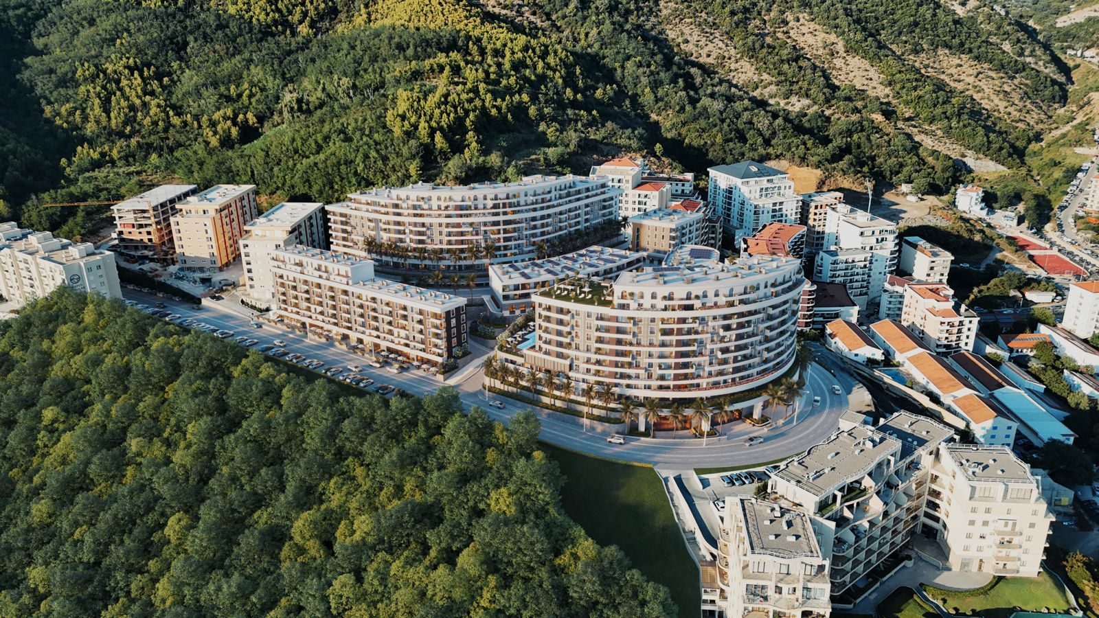 Aerial view of a modern residential complex in Bečići, Montenegro: multi-story buildings nestled among mountains and greenery.