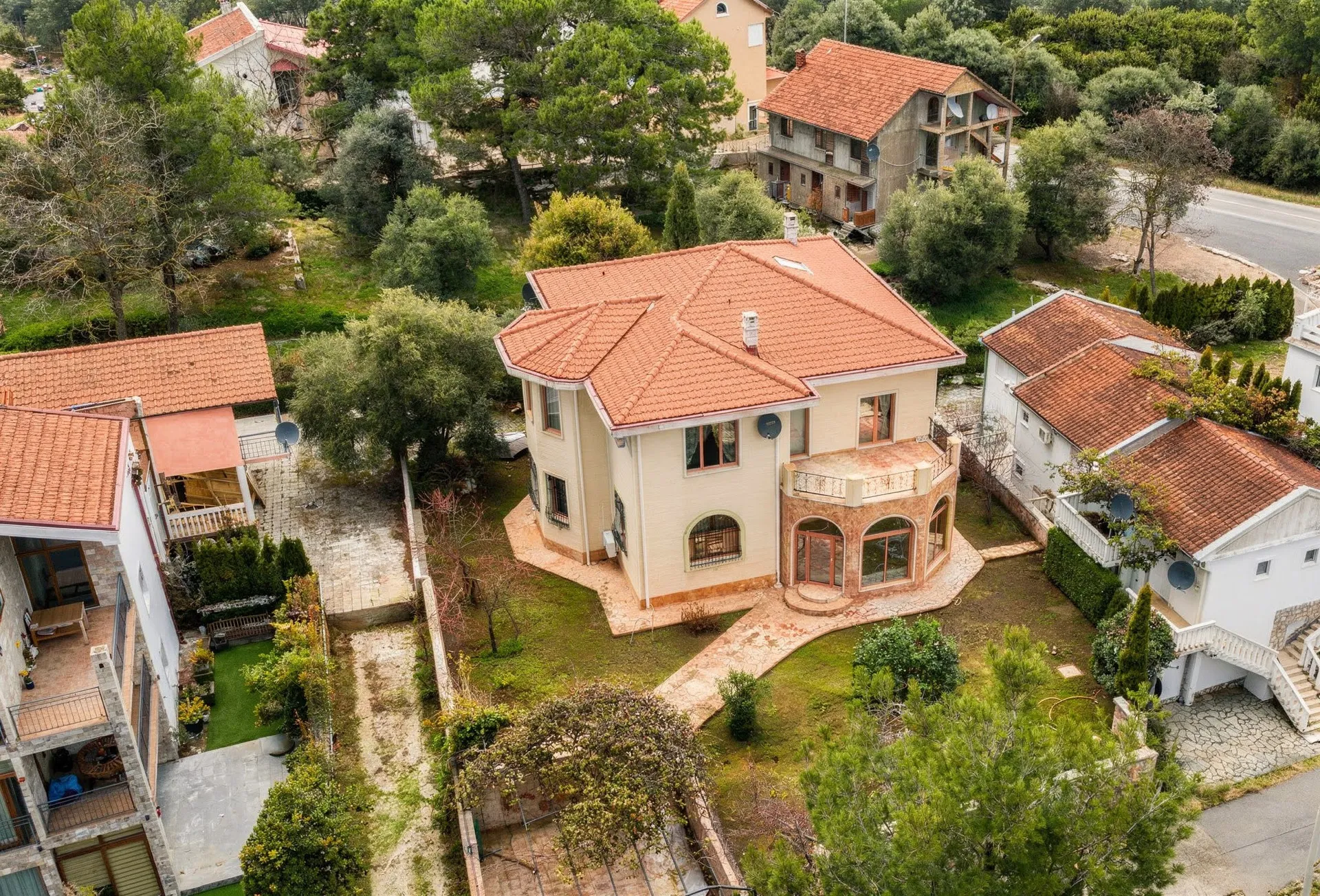 Aerial view of a two-story house with a red tiled roof and green garden surrounded by other buildings.