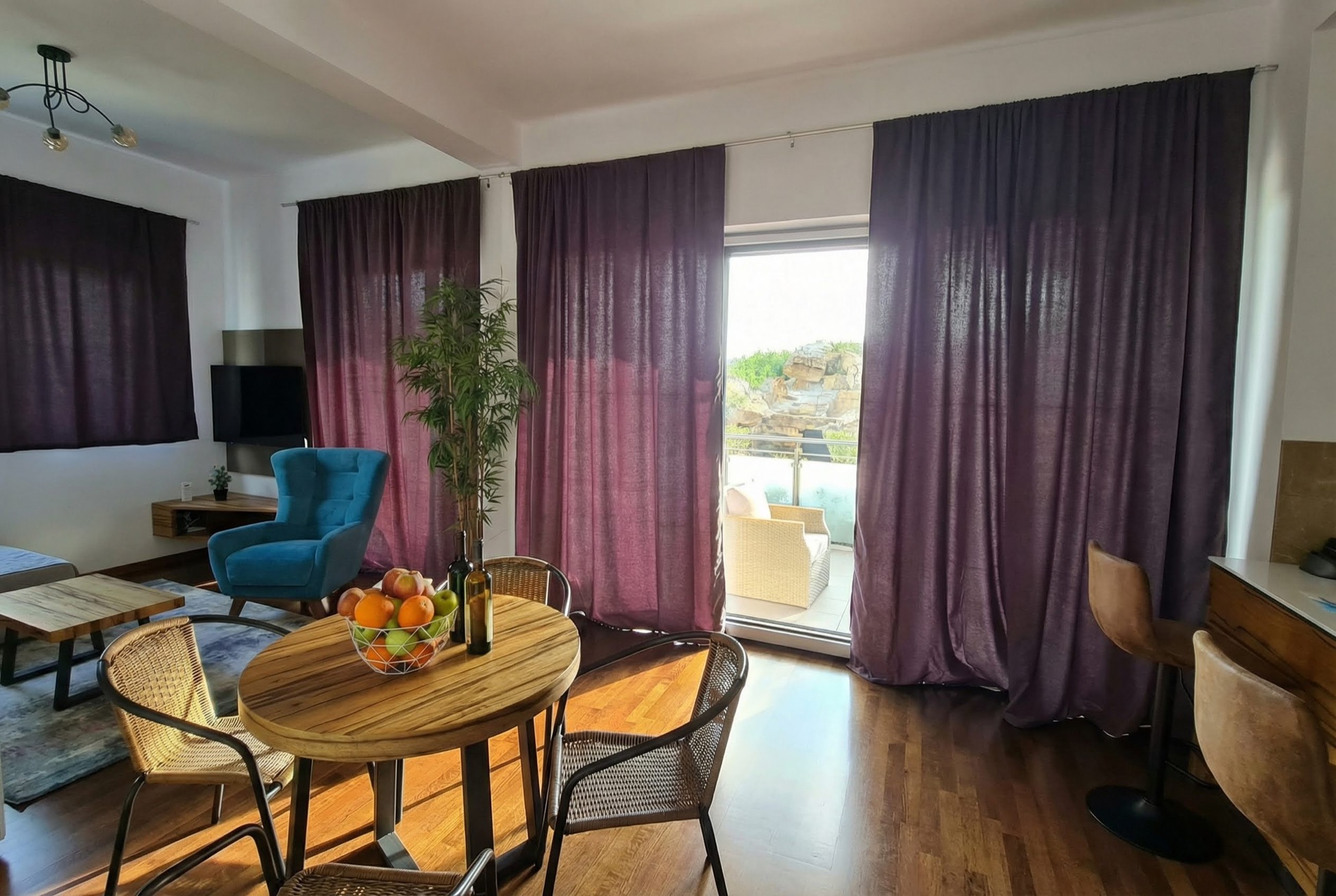 Living room in an apartment in Bečići, Montenegro: dining area, blue armchair, and access to a terrace with mountain views.
