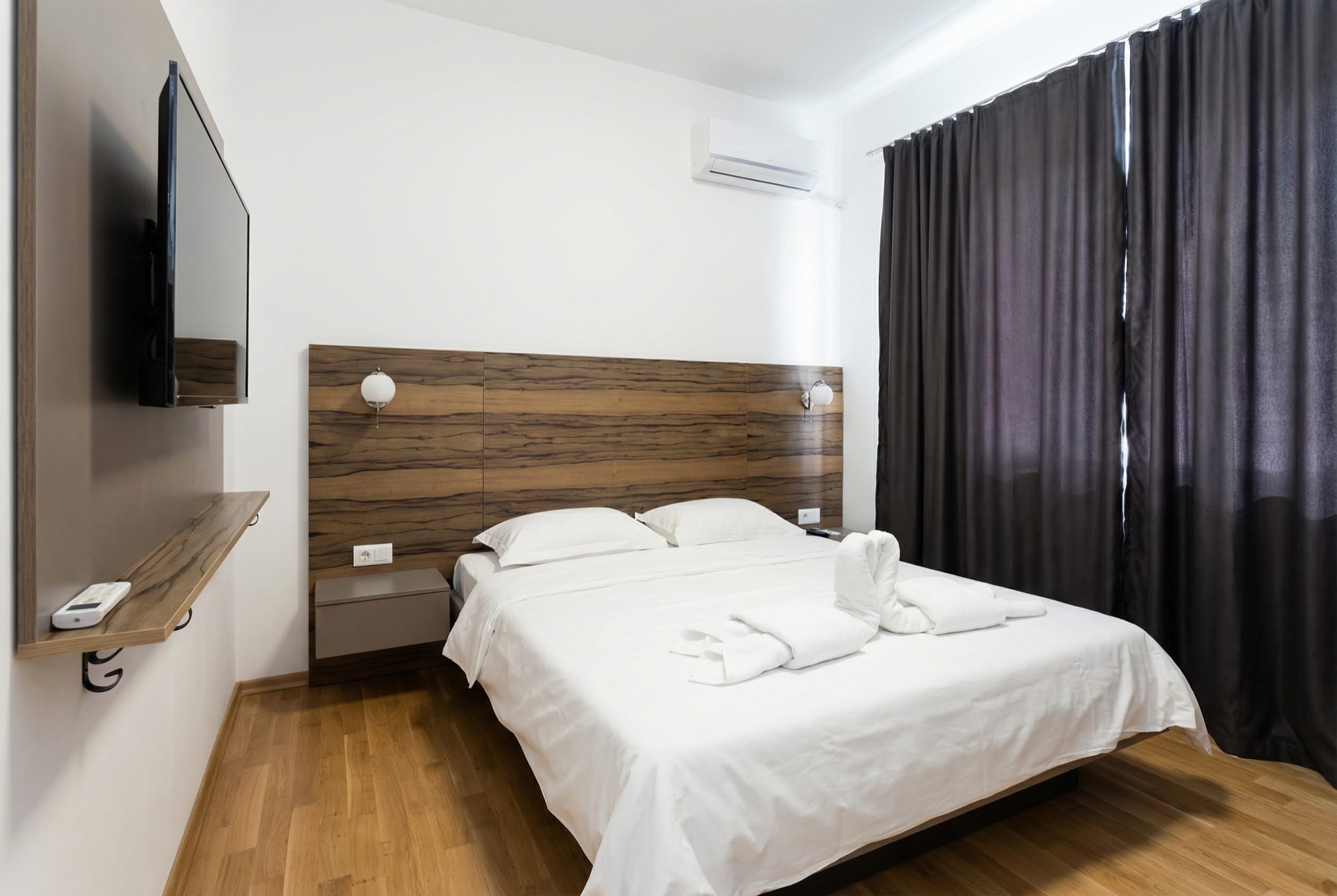 Modern bedroom in an apartment in Bečići, Montenegro: double bed, wooden headboard, TV, and air conditioning.