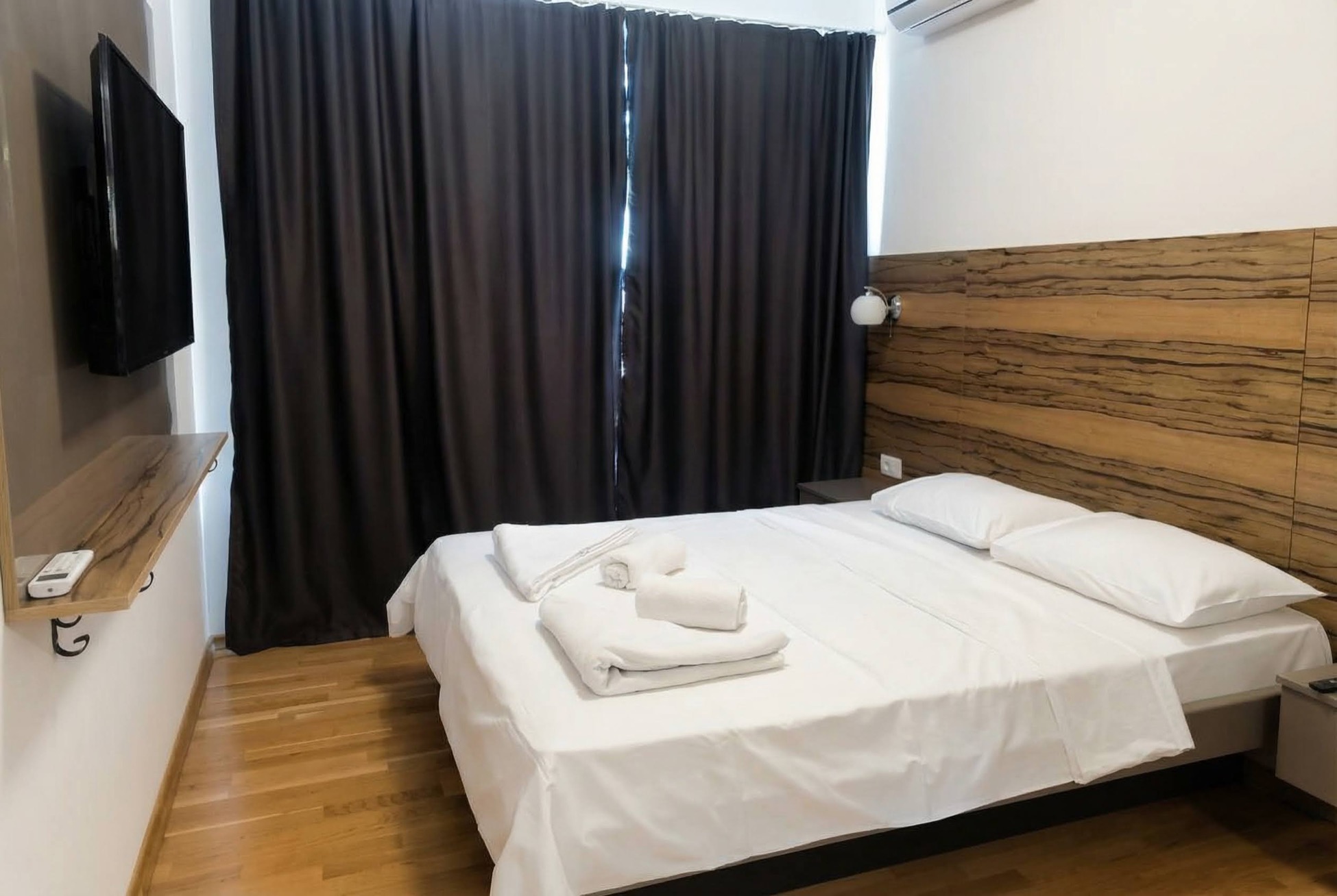 Bedroom in an apartment in Bečići, Montenegro: double bed, wooden wall paneling, TV, and parquet flooring.
