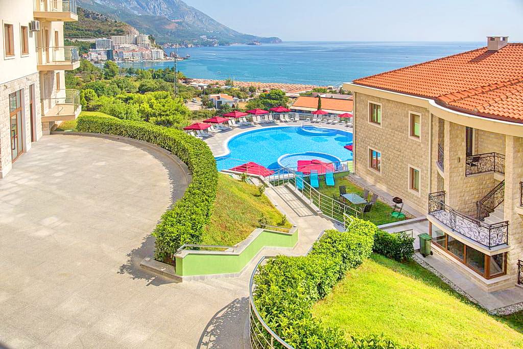 View of the pool and sea from the apartments in Bečići, Montenegro: a modern residential complex with a terrace and lounge area.