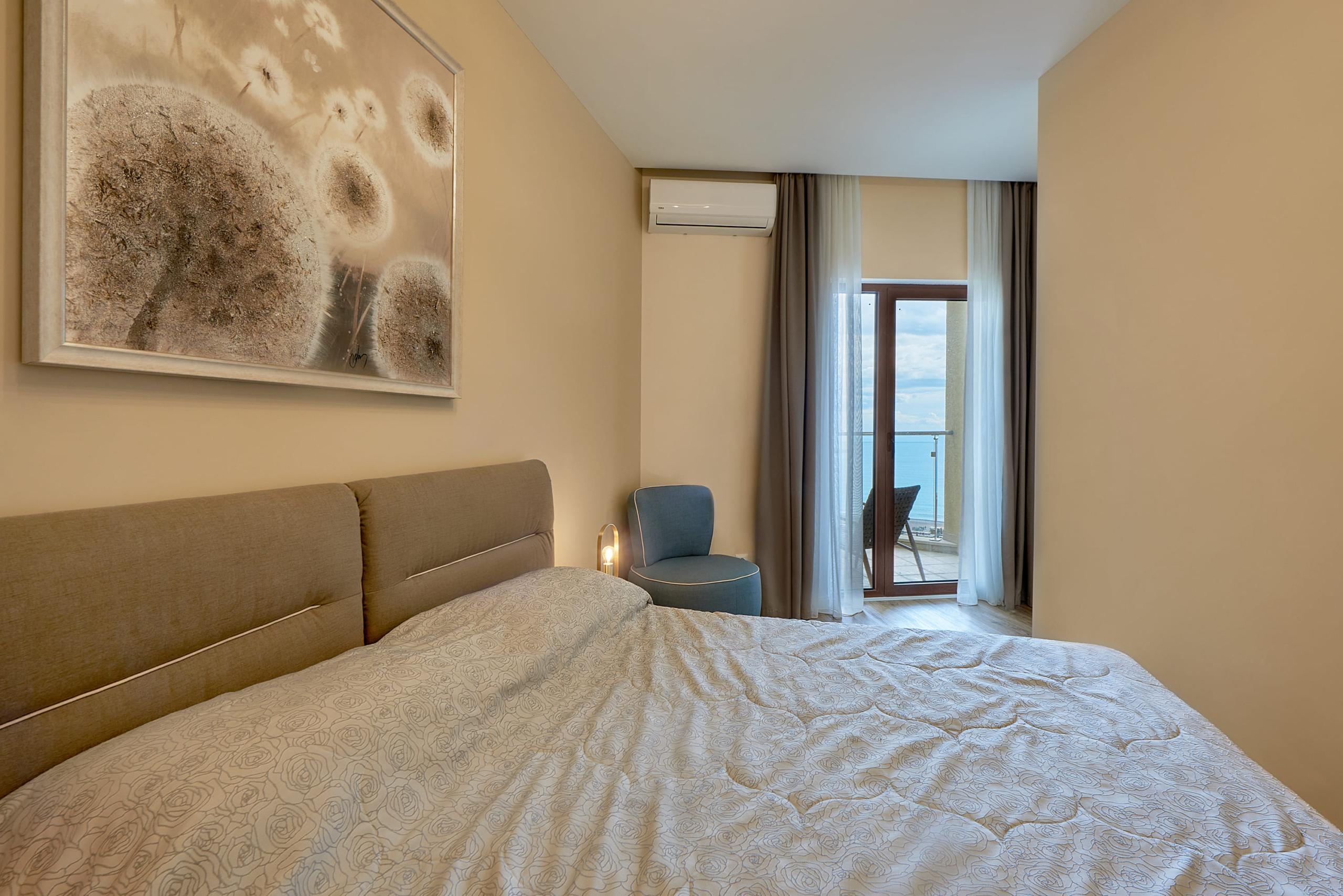 Bedroom in an apartment in Bečići, Montenegro: double bed, armchair, and access to a balcony with a sea view.