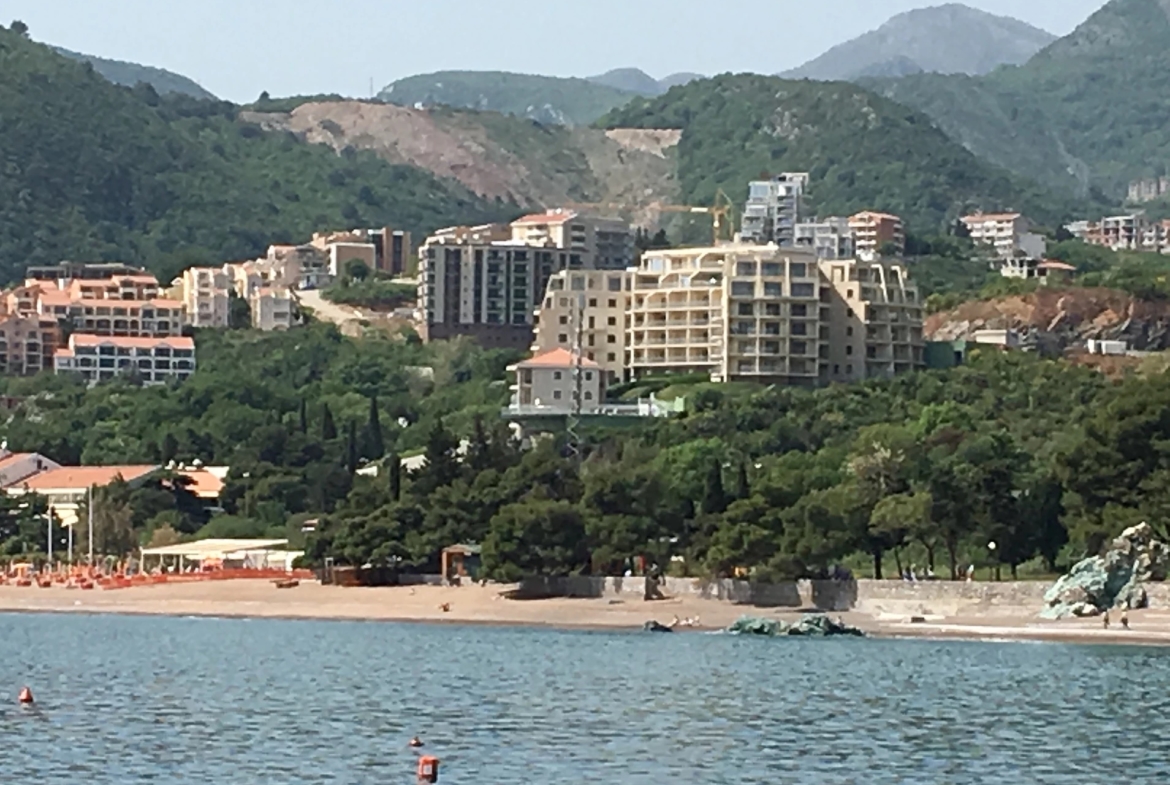 View of the residential complex and sandy beach in Bečići, Montenegro: modern seaside apartments against the backdrop of green mountains.