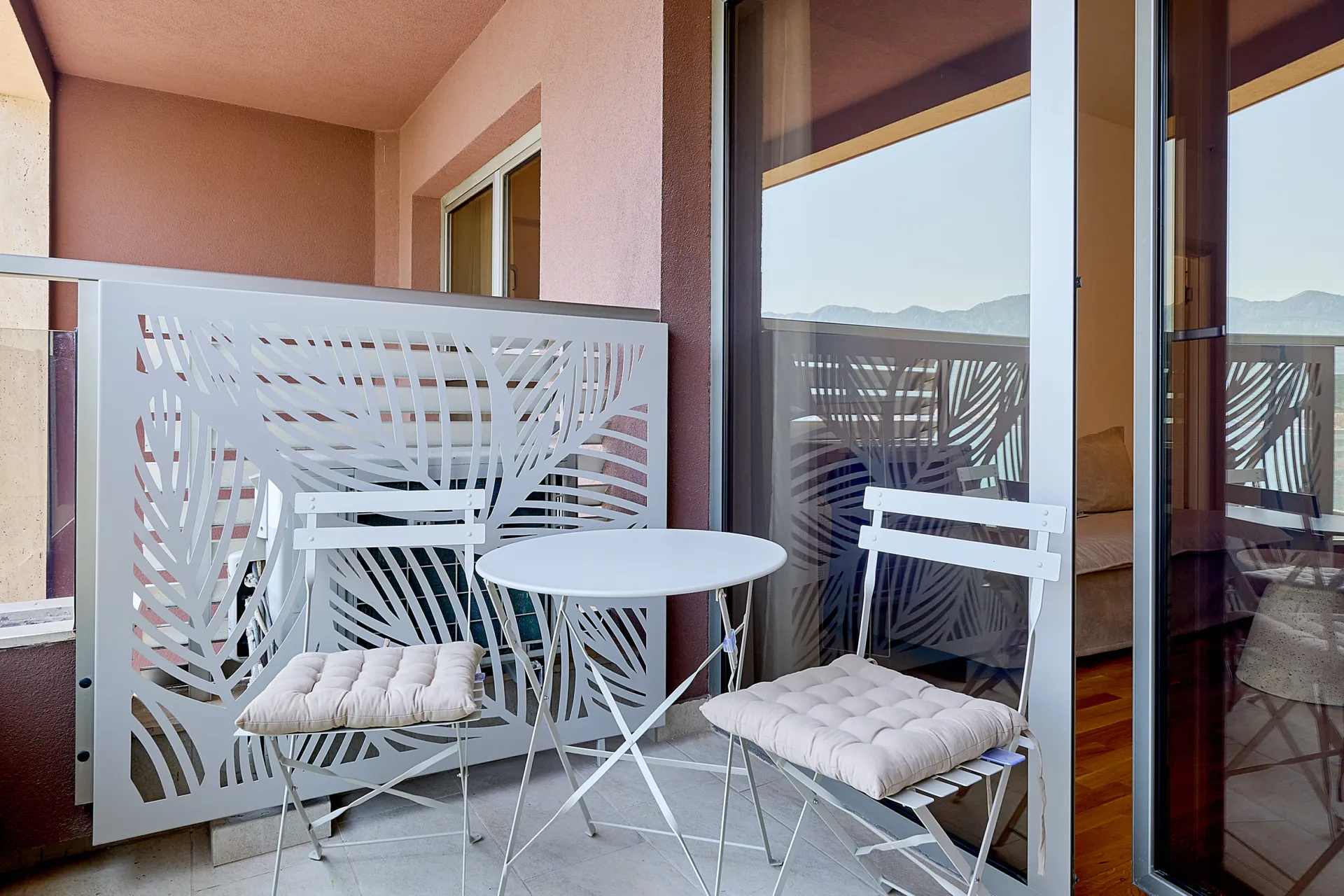 White balcony featuring a decorative leaf-pattern railing and small white table with cushioned chairs.