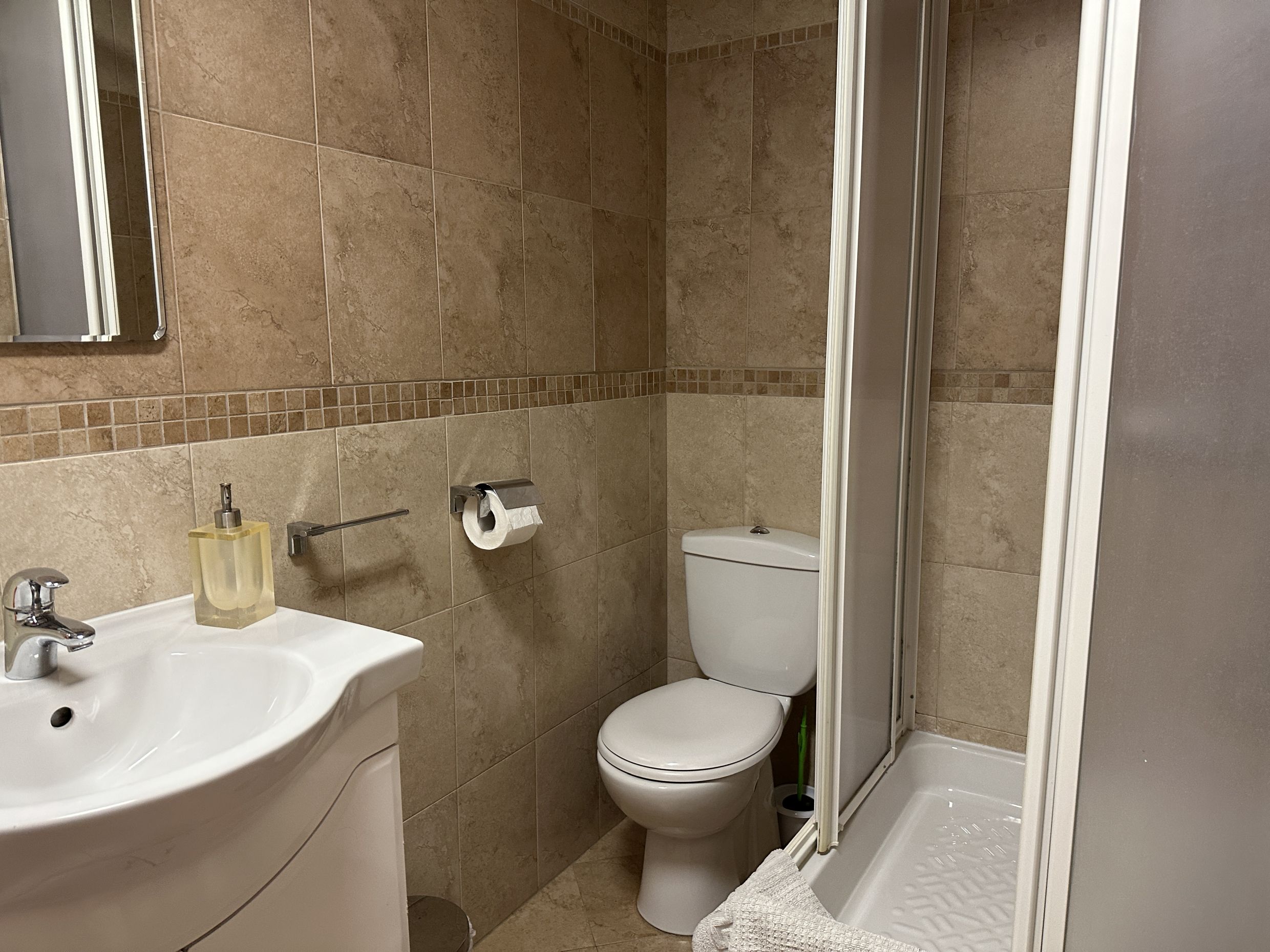 Bathroom in an apartment in Bečići, Montenegro: white sanitary ware, shower cabin, and beige tile finish.
