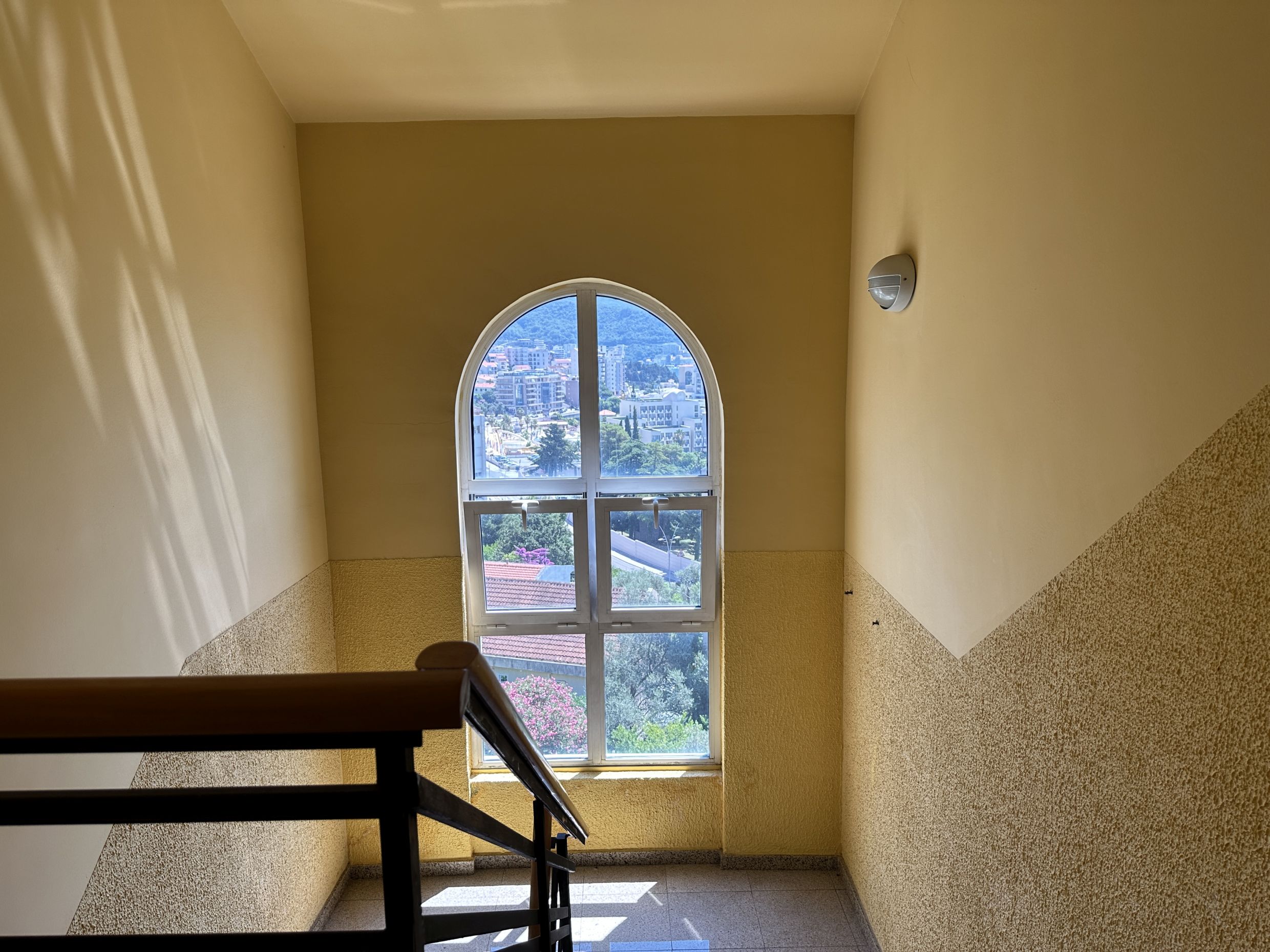 Arched window on the staircase with a view of Bečići, Montenegro, in a residential complex with wall finishing.