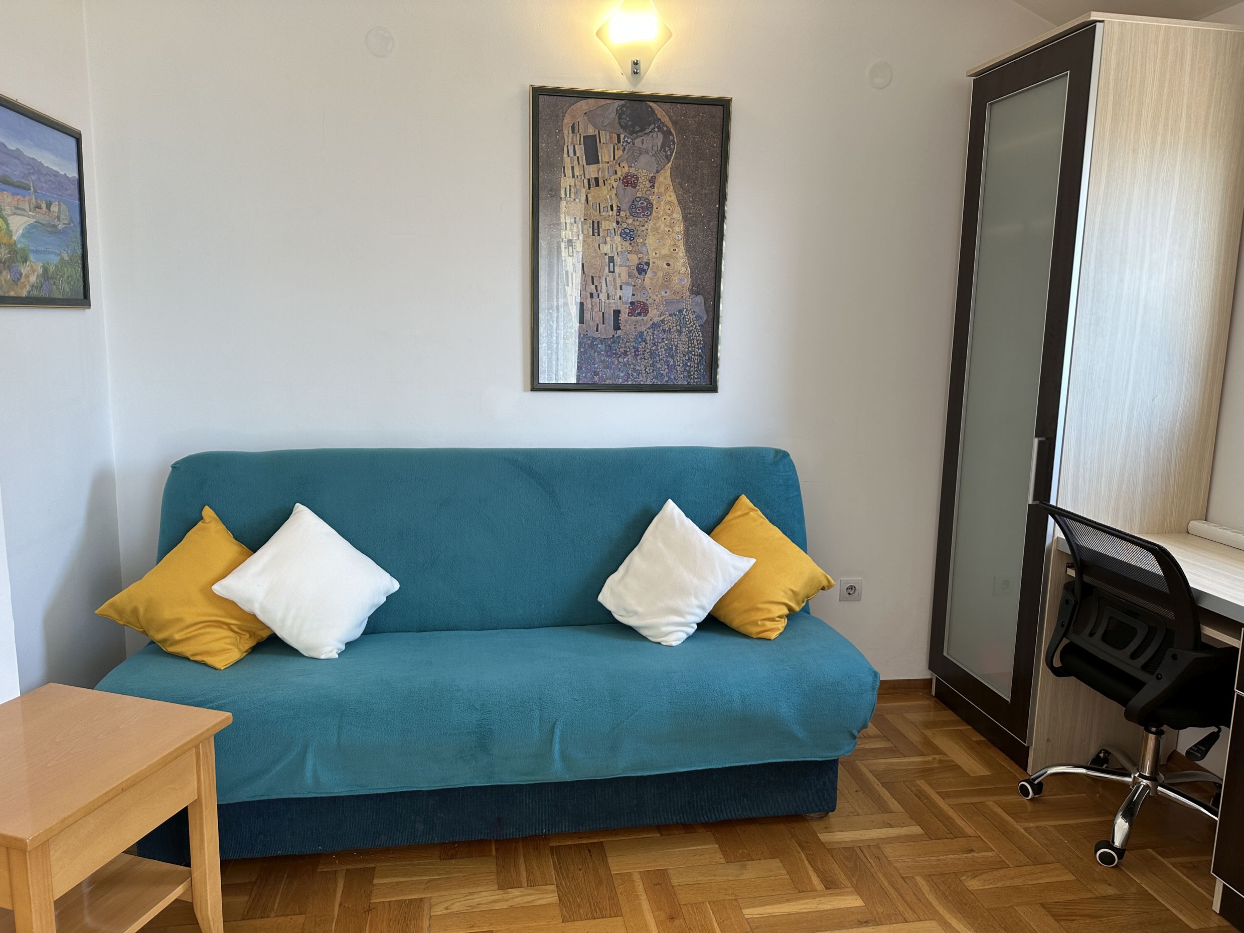 Living room in Bečići apartments, Montenegro: blue sofa, desk, parquet floor, and Gustav Klimt's painting The Kiss.