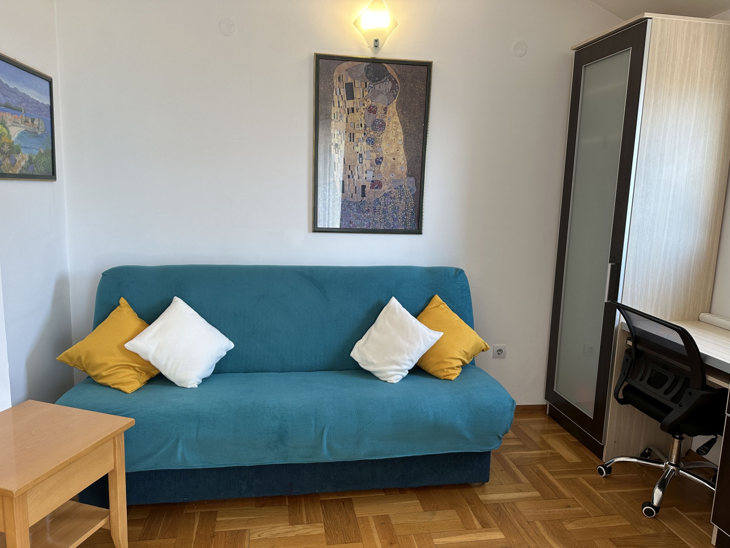 Living room in Bečići apartment, Montenegro: blue sofa with cushions, desk, and parquet flooring in the interior.