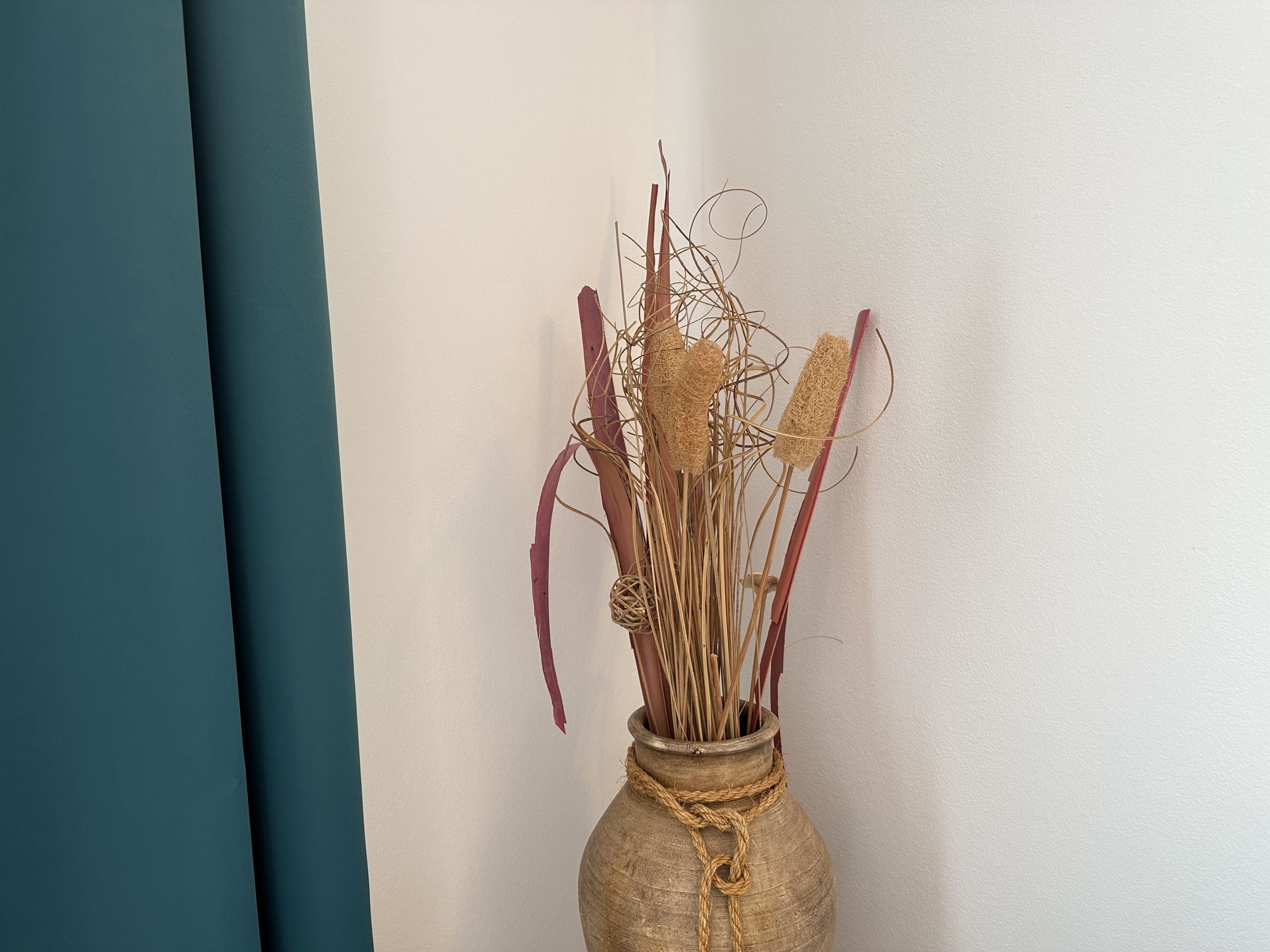 Apartment interior decor in Bečići, Montenegro: a ceramic vase with dried flowers against a white wall and blue curtain.