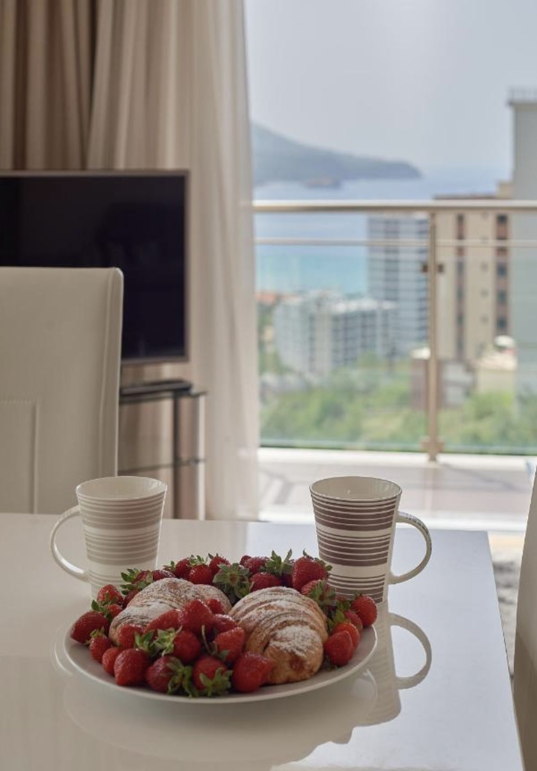 Breakfast with strawberries in the living room of an apartment in Bečići, Montenegro, with a panoramic view of the sea and mountains.